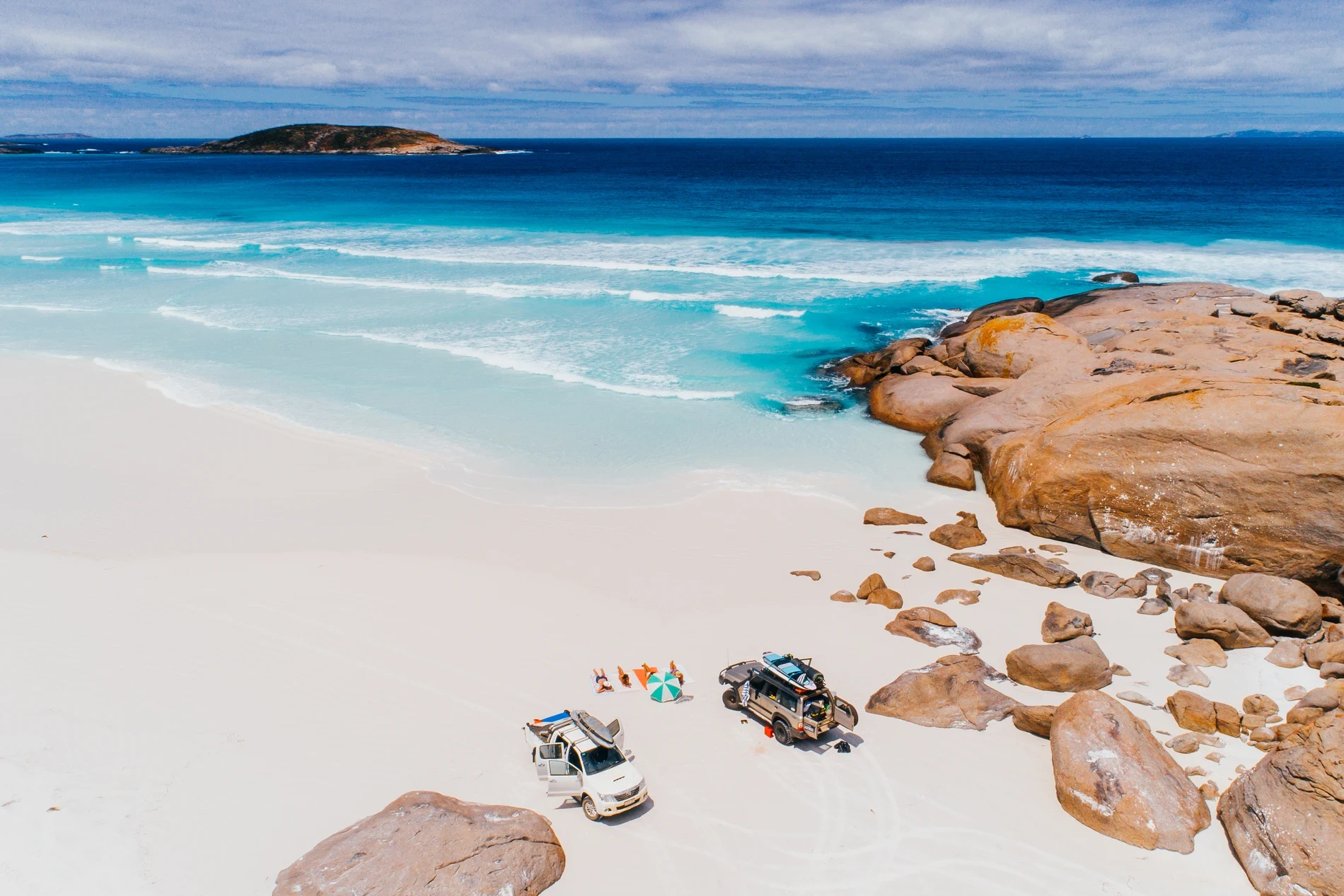 Vehicles and camp set up on a white beach beside granite boulders and clear water