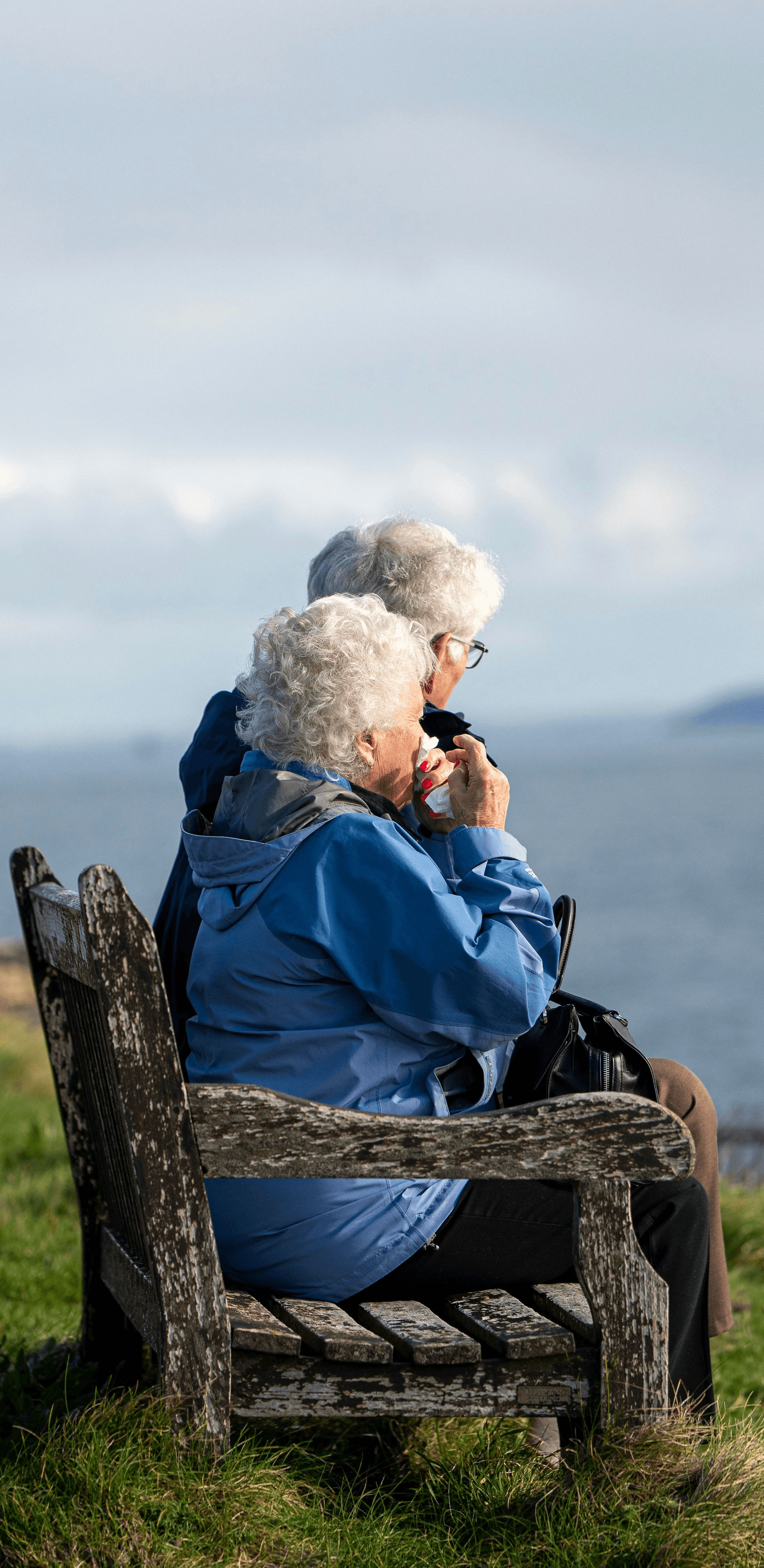 man and woman sitting on gray wooden bench viewing blue sea during daytime