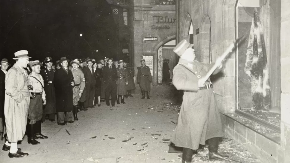 People watch as a Nazi official attacks a Jewish business - YAD VASHEM PHOTO ARCHIVE