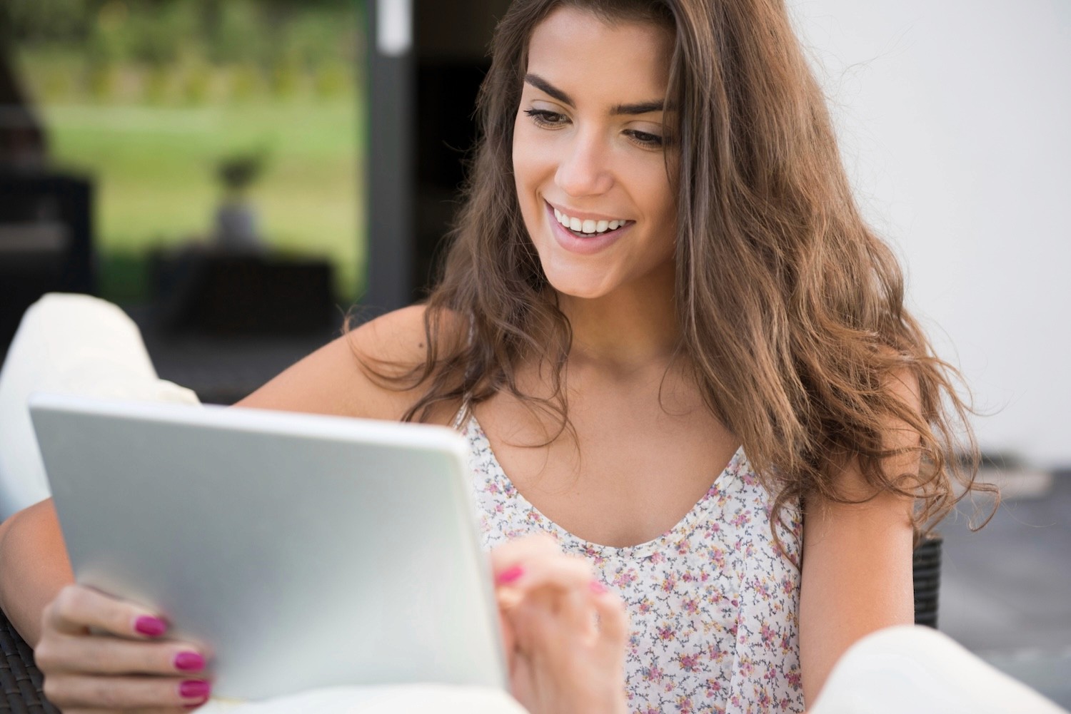 Frau mit langem Haar und geblümtem Top sitzt vor einem Laptop und tippt auf der Tastatur