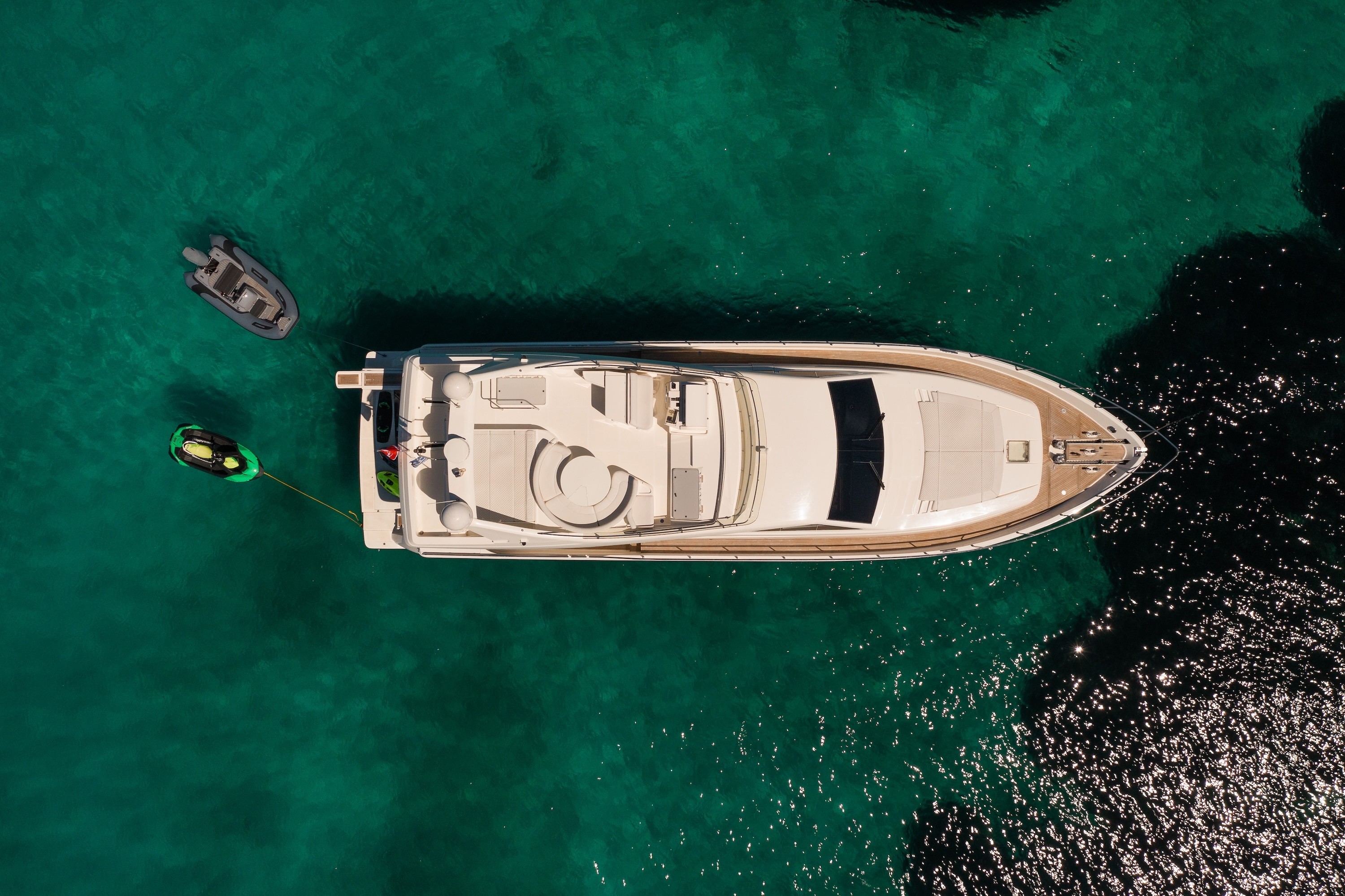 Aerial view of luxury motor yacht Ferretti 68 anchored in crystal-clear turquoise waters with tender boat and water toys nearby.