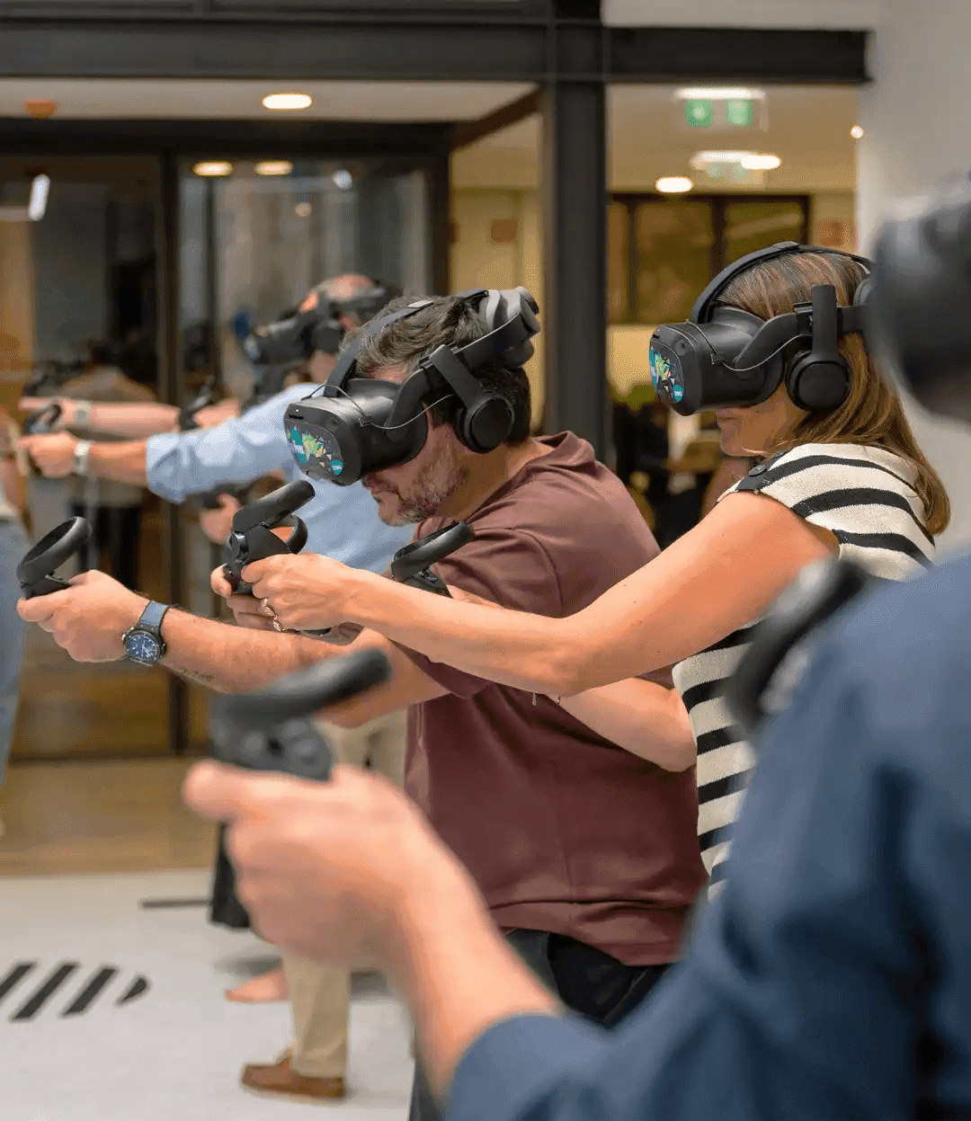 A group of people wearing VR headsets and holding controllers, standing together and preparing to enter the virtual reality arena as a team.