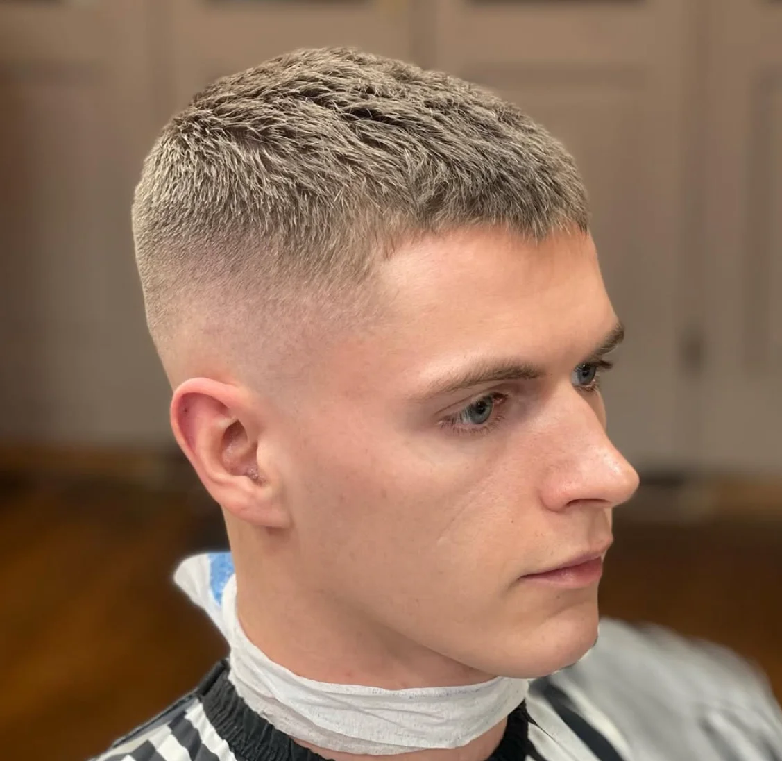 Young man with a precisely styled haircut, seated in a premium barbershop setting.