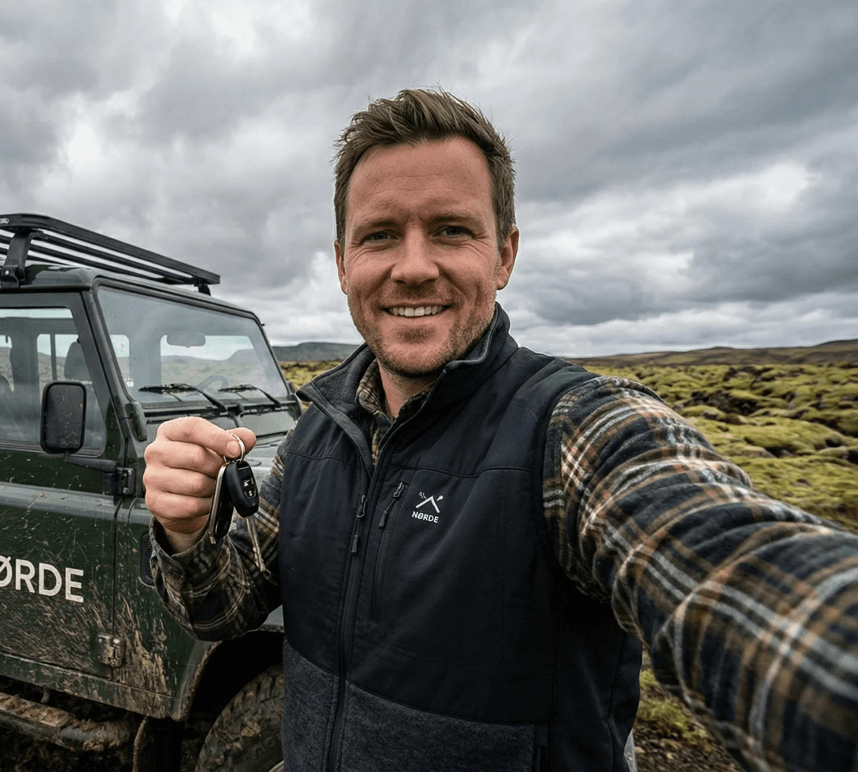 Smiling man holding a car key in a green, natural setting.