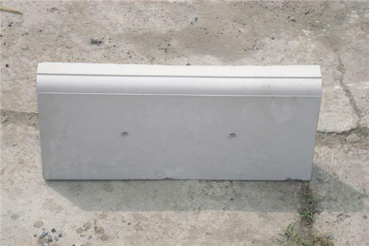 A single concrete curb stone with a clean, polished surface and a rounded edge on one side, resting on a concrete floor. The design suggests it is for outdoor use in landscaping or street construction.