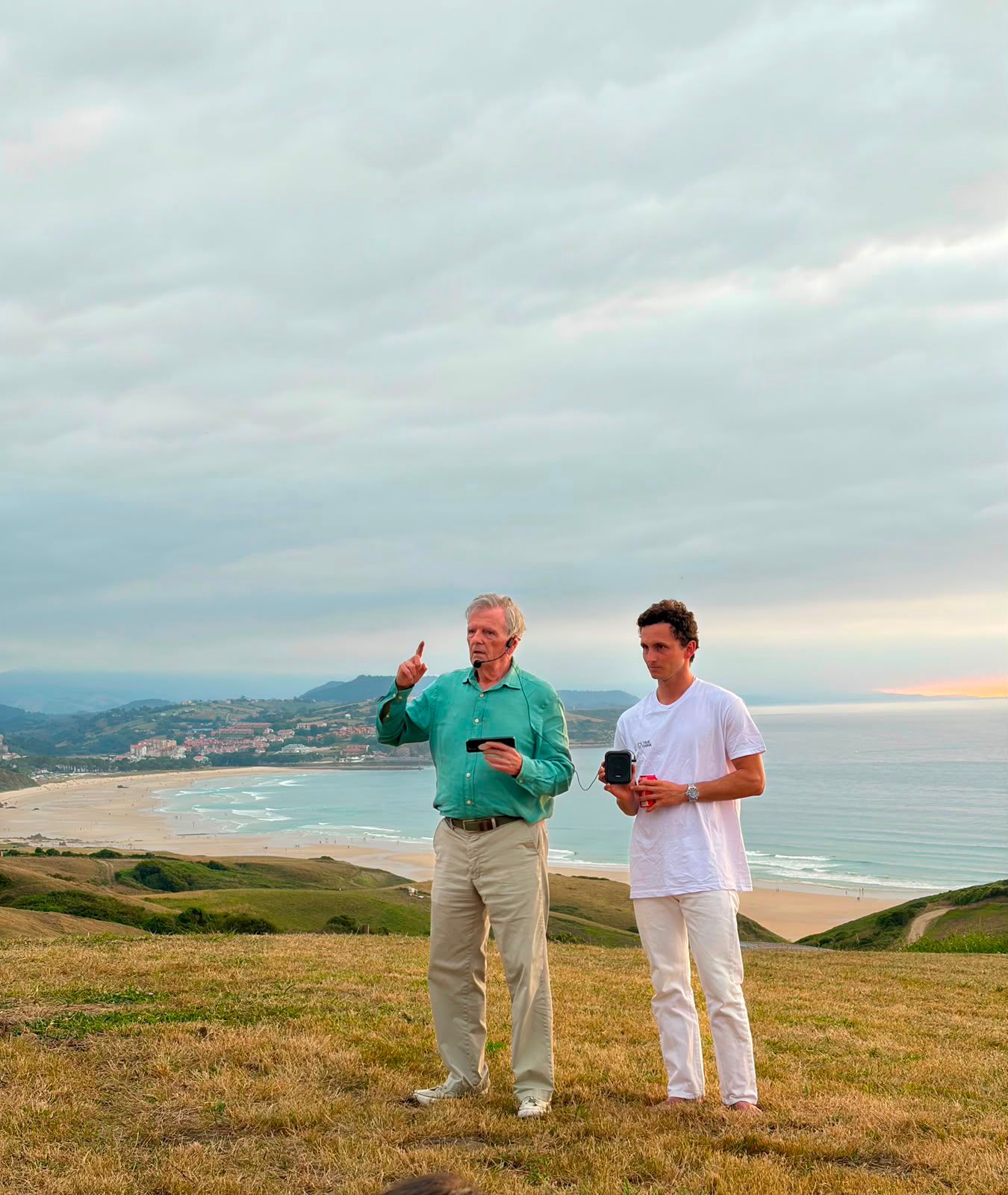 Tomás Alfaro señala el horizonte junto a un alumno, sobre las dunas y la playa de El Rayo Verde en Cantabria