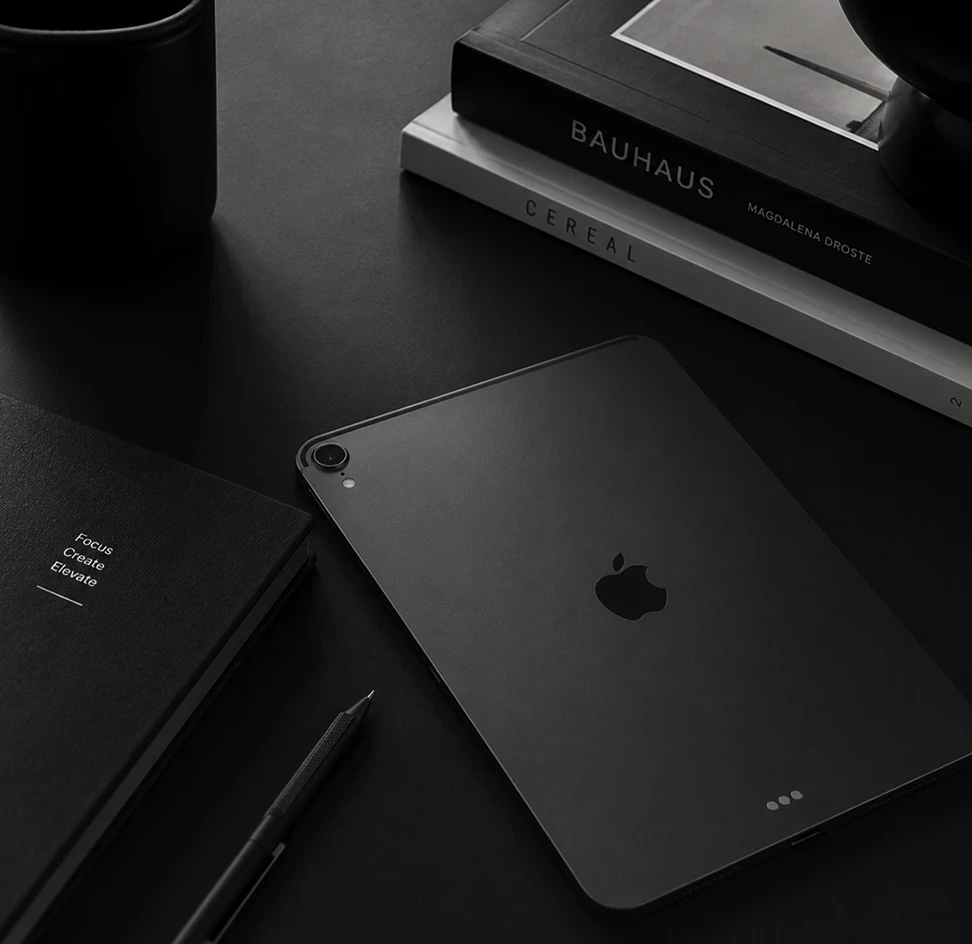 Design workspace flat-lay showing an iPad Pro, Bauhaus and Cereal design books, a notebook, and a pen on a dark surface