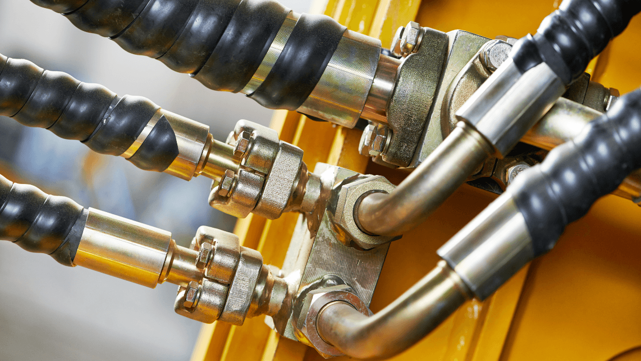 Close-up van hydraulische slangen en metalen koppelingen op industriële machine, gebruikt voor kracht- en drukoverdracht in hydraulische systemen binnen de industrie en machinebouw.