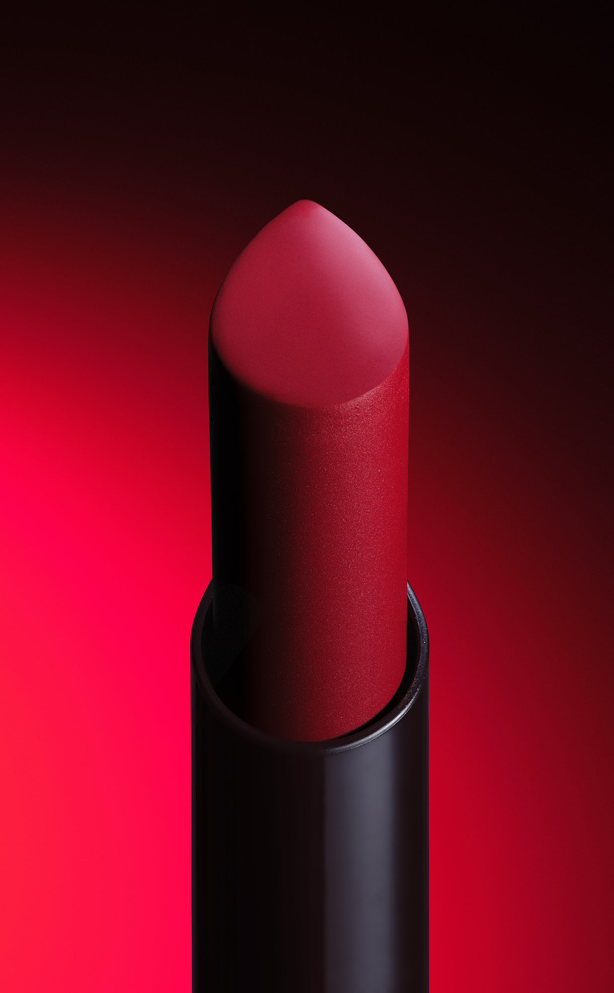 Vibrant red lipstick in sleek black tube against a bold red gradient background.