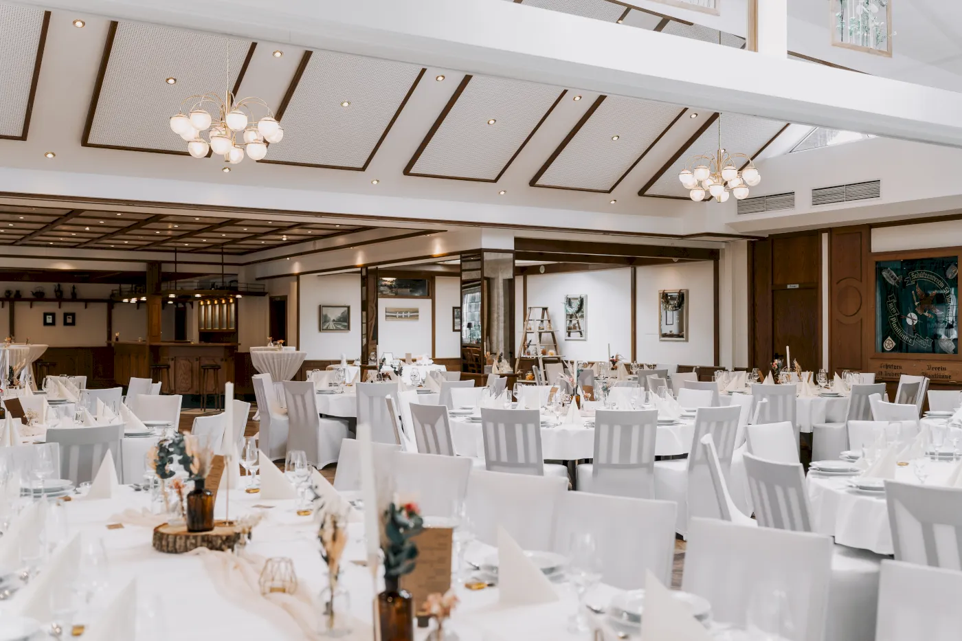 Großer Saal für Hochzeitsfeier mit runden Tischen, weißen Stühlen und eleganten Dekorationen.