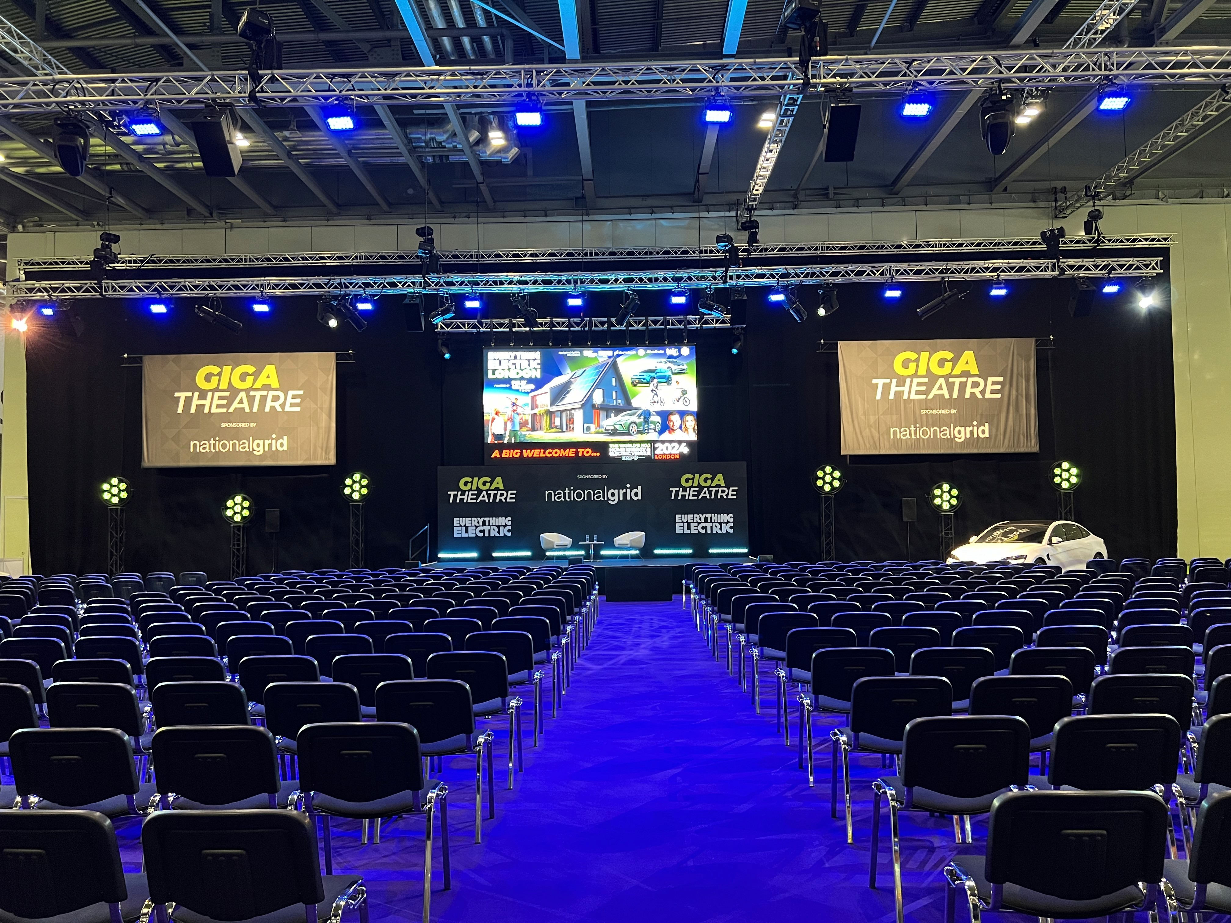 Giga Theatre at Everything Electric London with a large stage, truss, presentation screens, event lighting and audience seating.