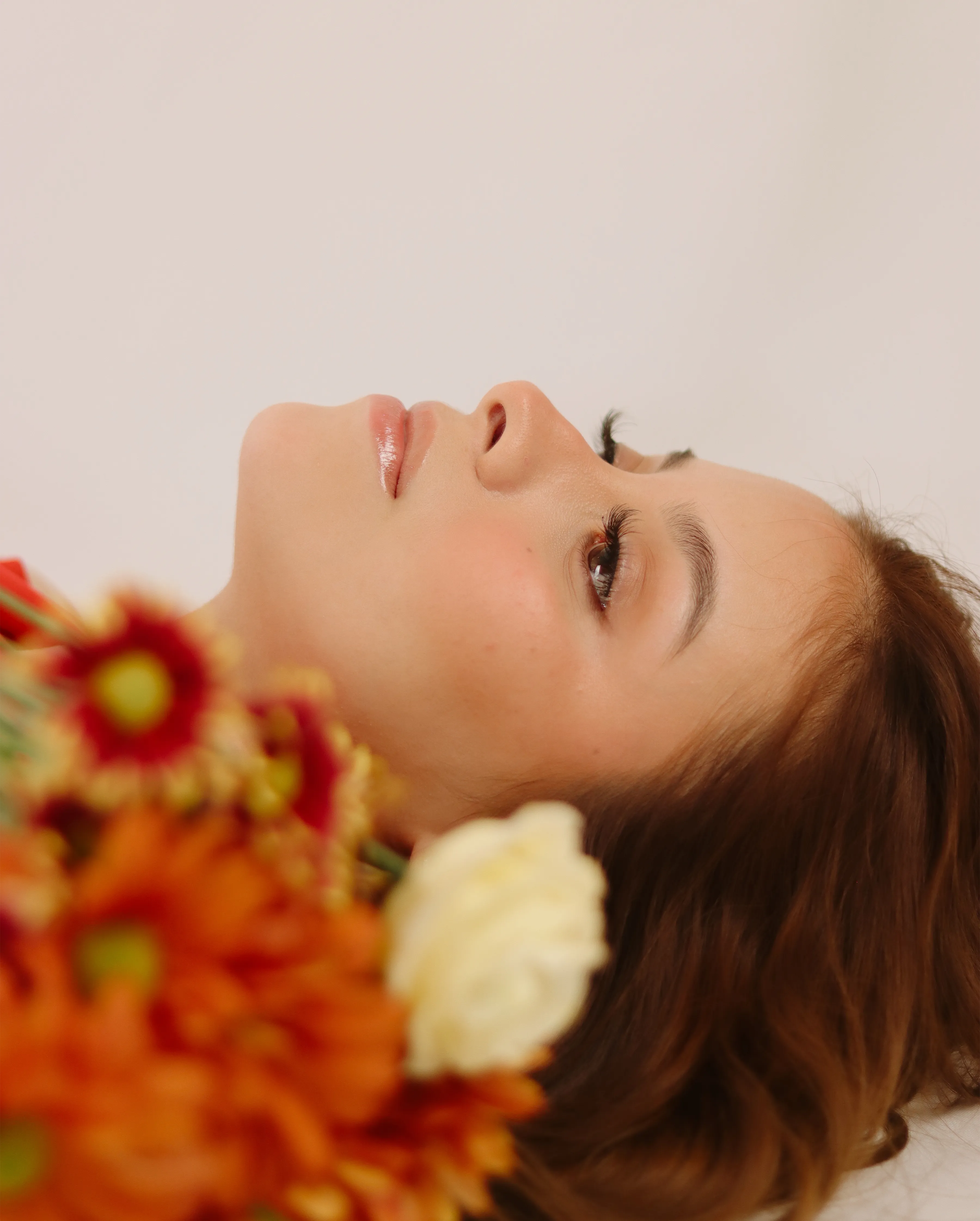 Mujer recostada sosteniendo flores naranjas junto al rostro