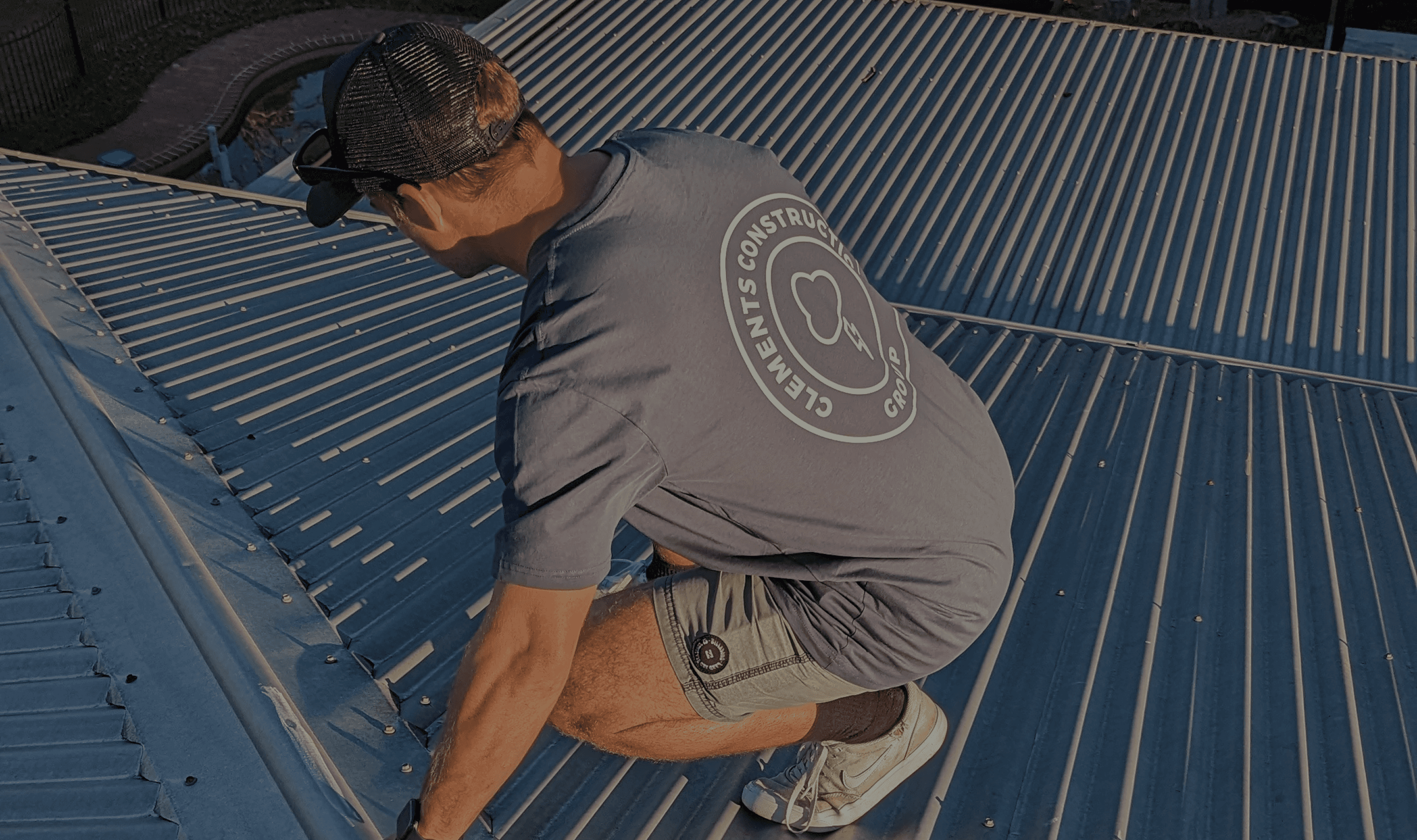 Construction worker on a metal roof inspecting storm damage, with Clements Construction Group branding visible.