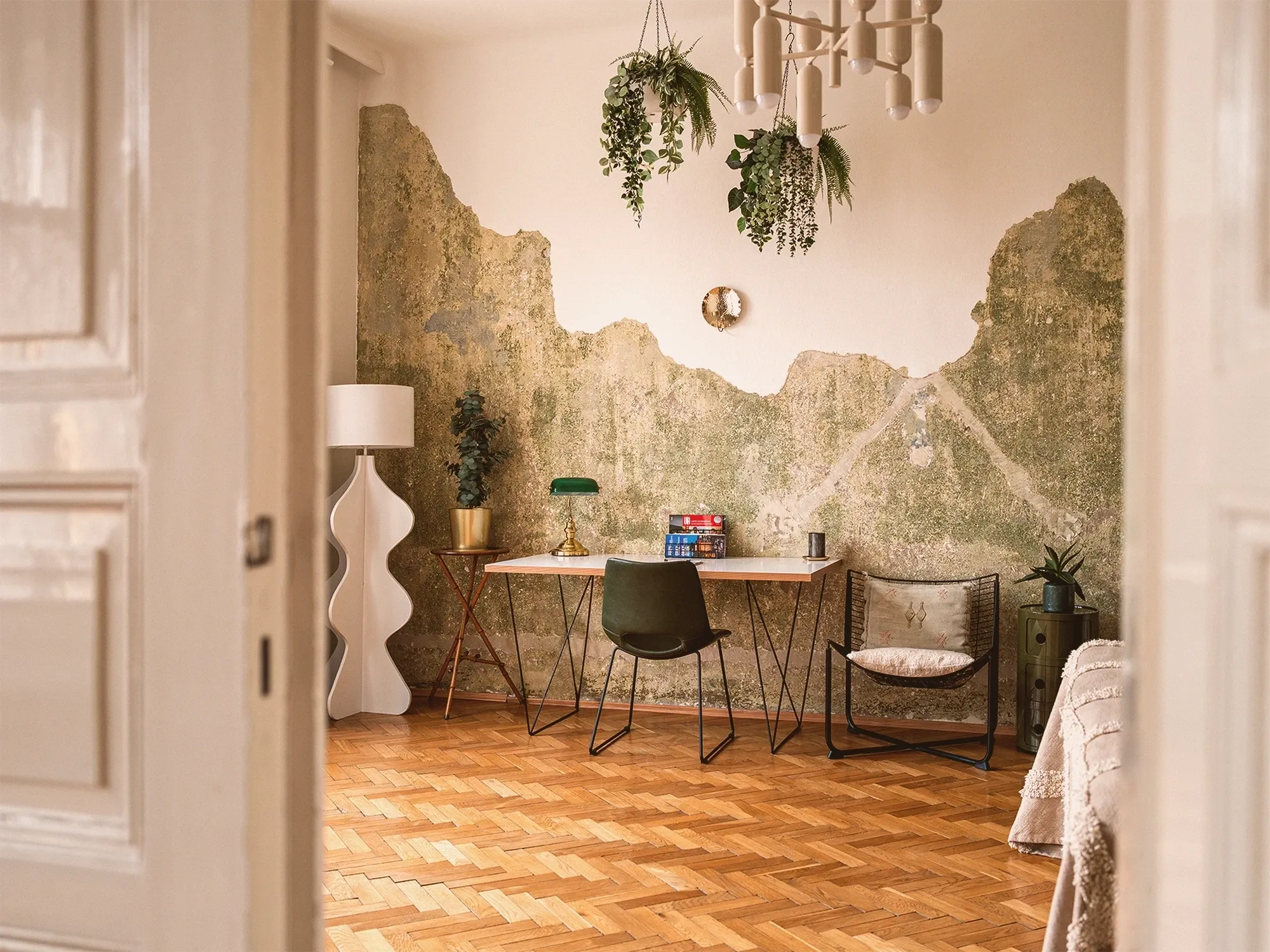 Sunlit apartment interior with herringbone parquet floor, tall windows and a wooden desk with a white lamp