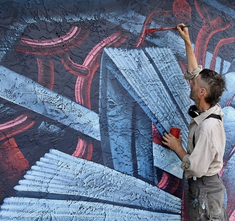 A painter brushes red lines over a mural of pale blue petals.