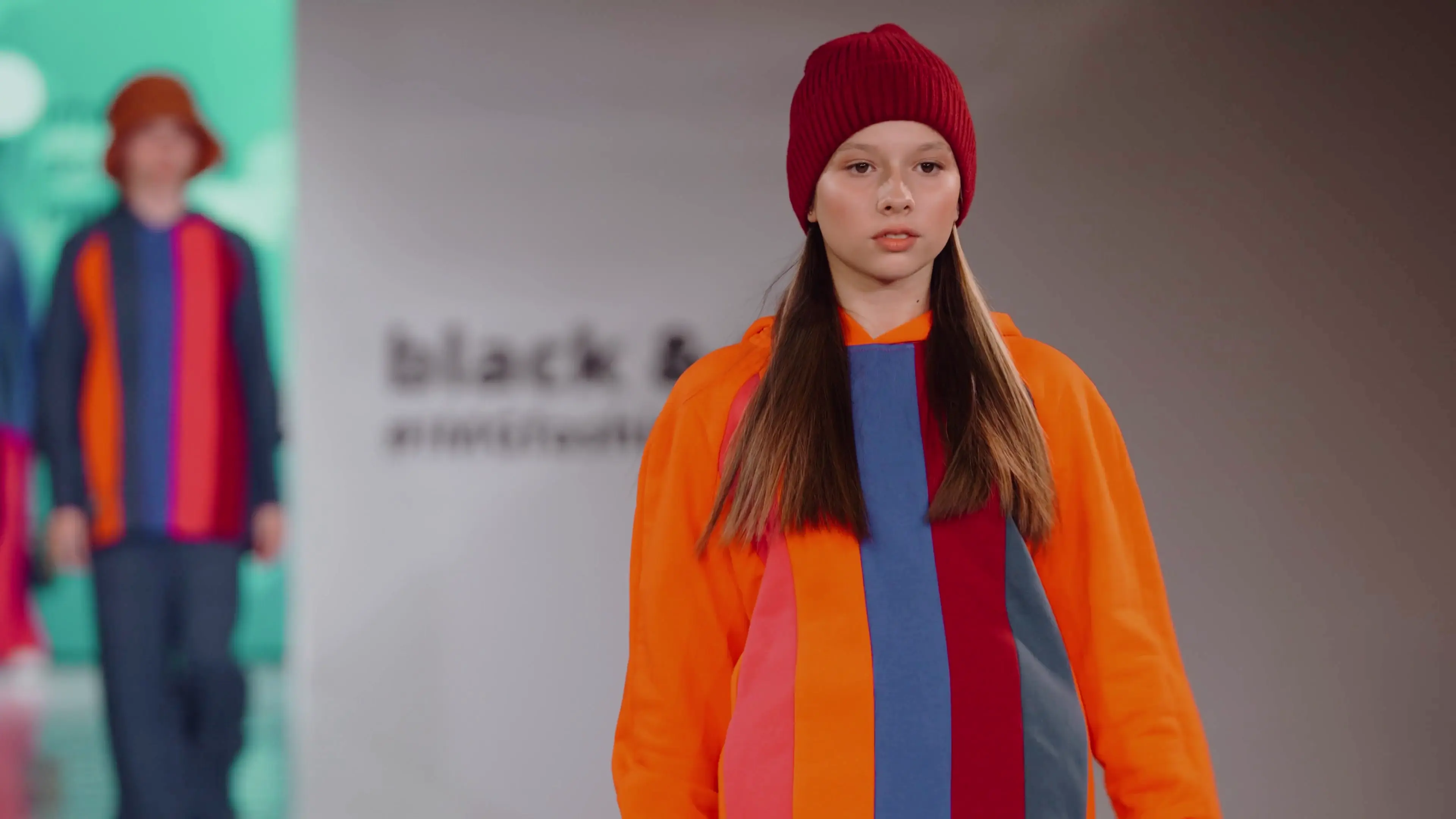 A girl in an orange jacket and red hat at a fashion show