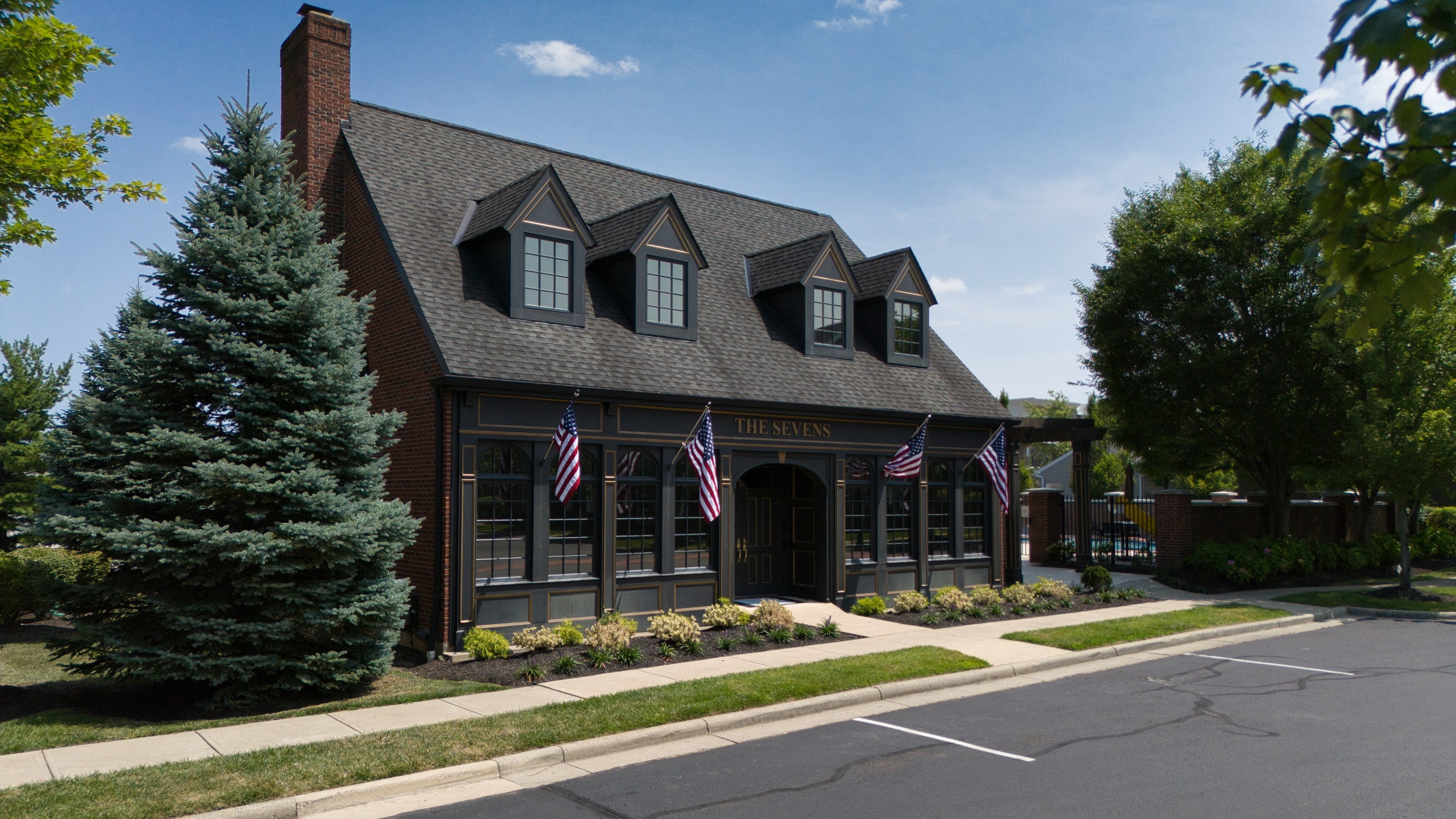 A modern house with a dark exterior, featuring multiple roof peaks and surrounded by trees and landscaping.