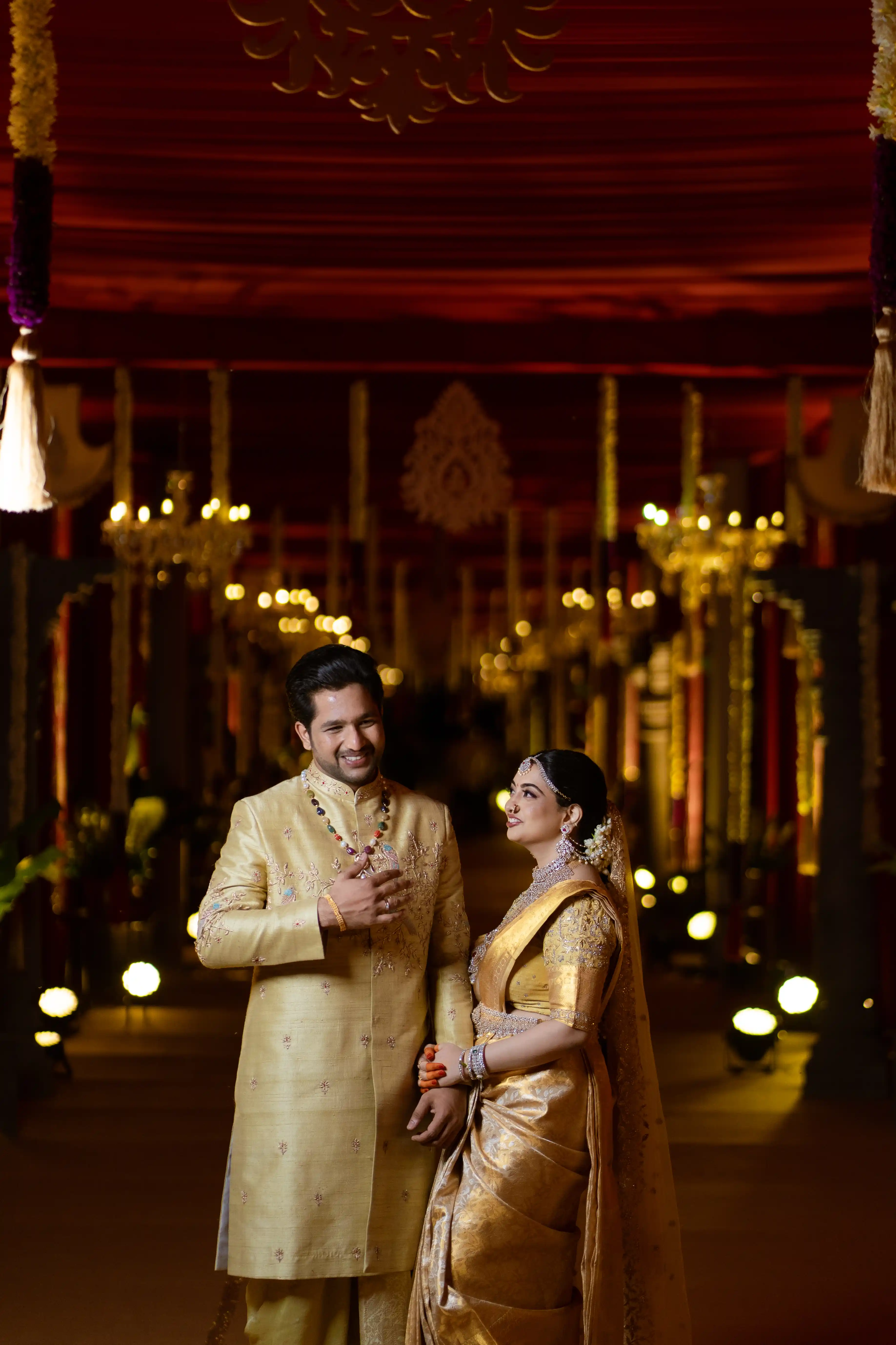 A couple in elegant traditional Indian outfits stands together, beaming for the camera and celebrating their rich heritage. Photo by Out of The Blues Fine Art Wedding Photography in Hyderabad.