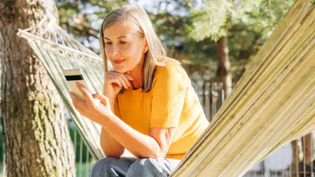 Ein Frau sieht in ihr Smartphone und überlegt sich, ob sie trotz Allzeithochs investieren soll