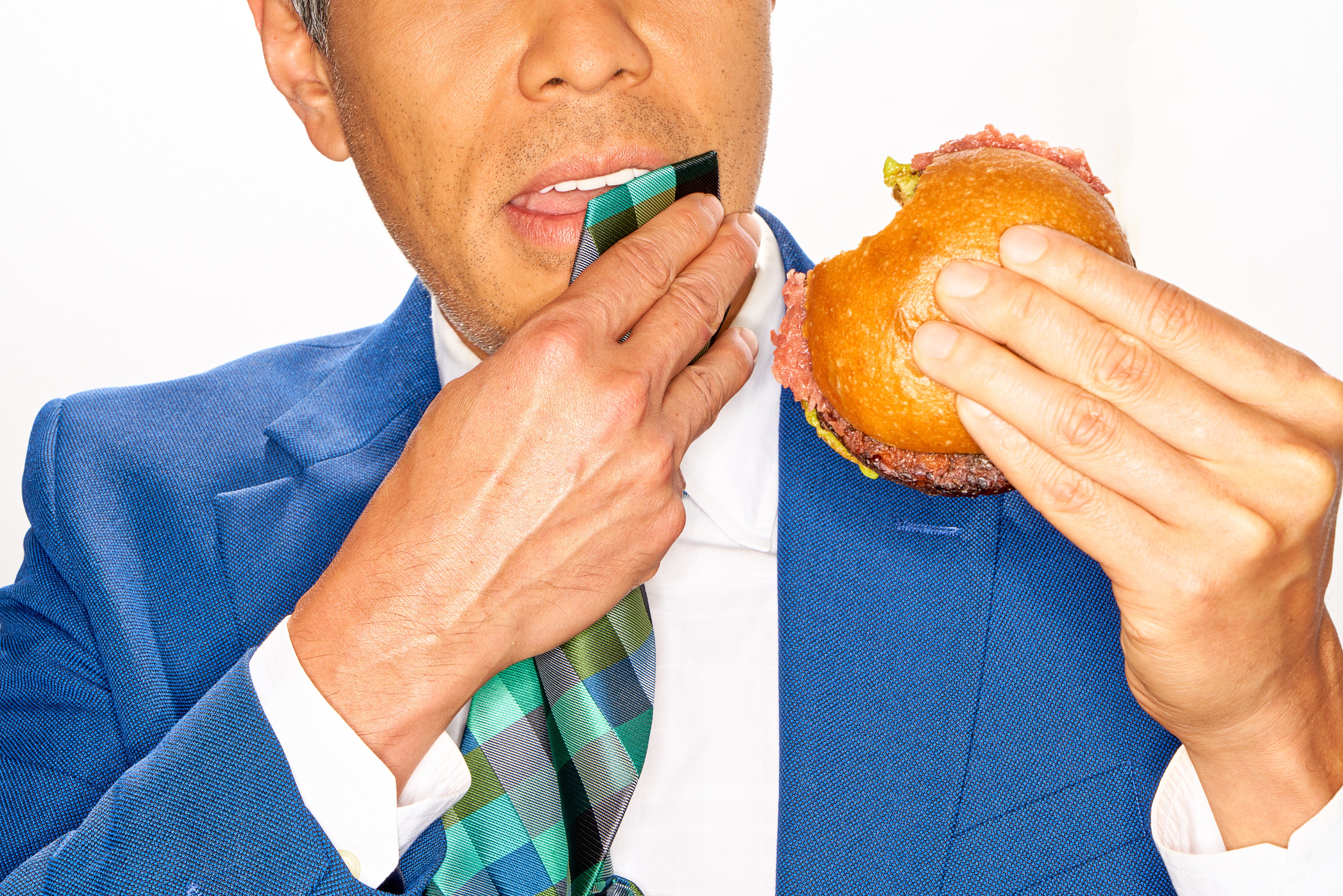 Talent in a vivid blue suit holding a Kernel burger and patterned necktie