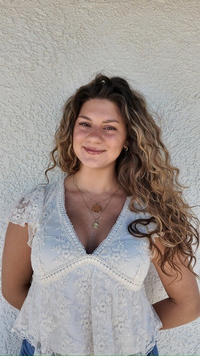 Portrait of Alexis Hedley, Campaign Manager at Playkit, smiling in front of a beige wall and wearing a black strapless top with a gold cross necklace.