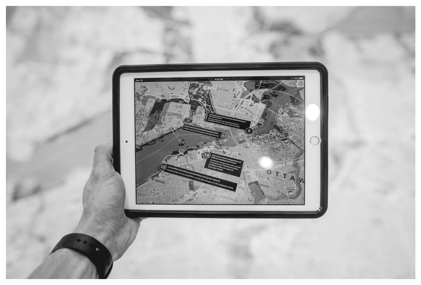 Hand holding tablet displaying real-time freight tracking map with numbered delivery points and route information overlaid on city streets, demonstrating modern TMS visibility features for load tracking and customer updates