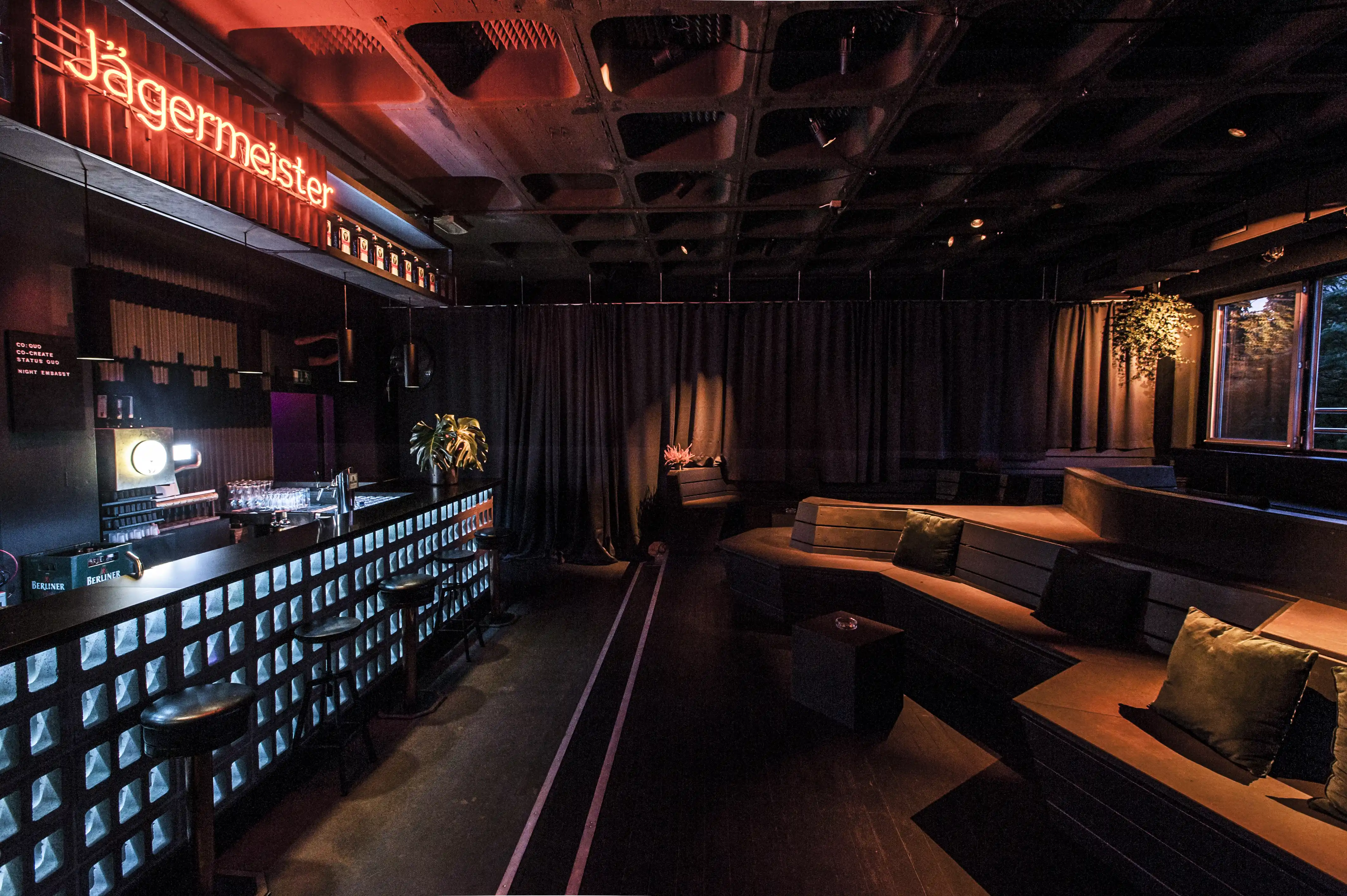 Lounge of the Jägermeister Night Embassy with dark daybeds and the glowing bottle-crate bar under the orange neon lettering.