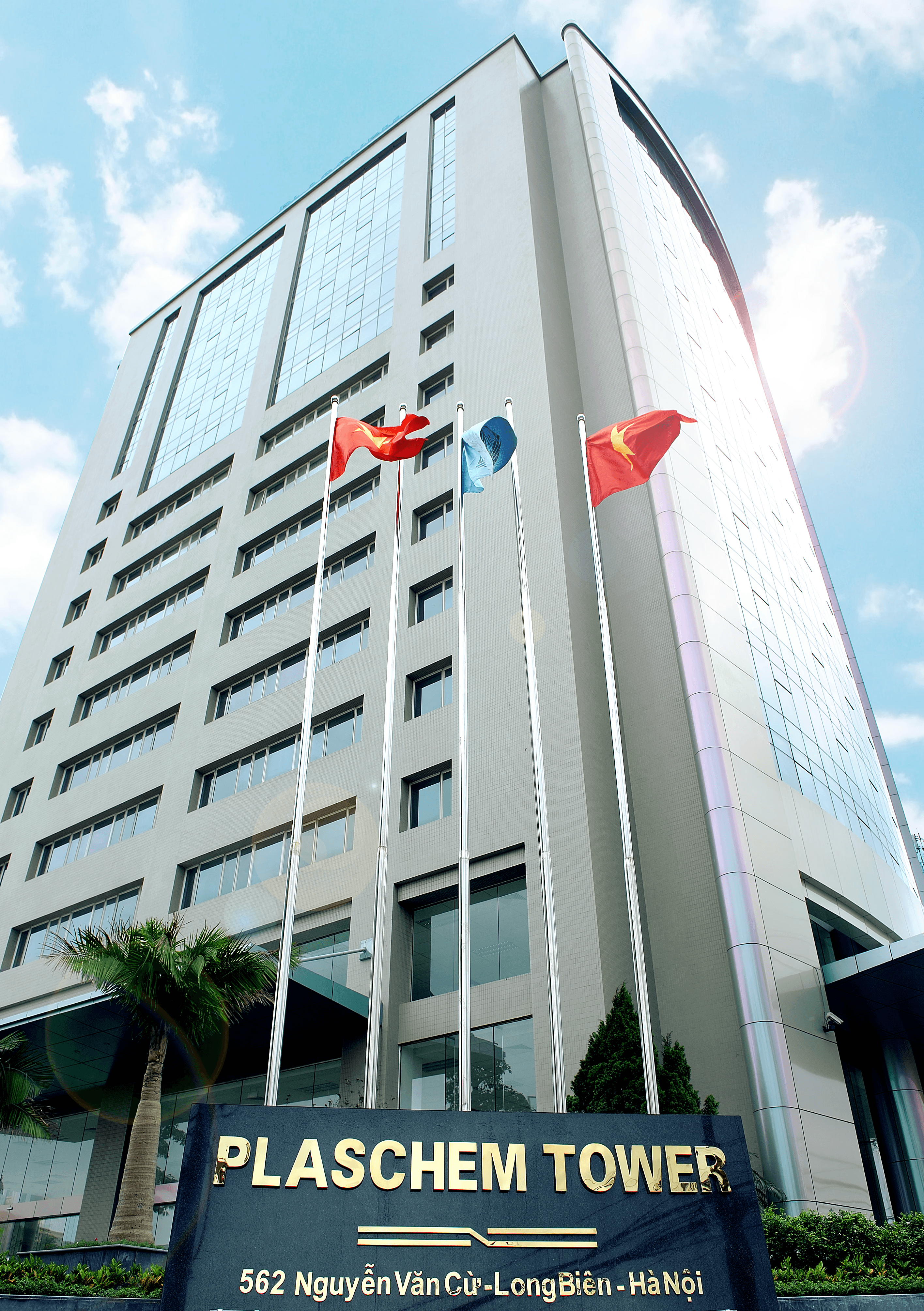 A tall modern building with flags displayed, set against a blue sky and green landscaping.