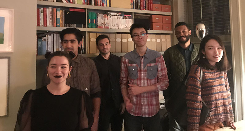 A photo of a group of people sitting in a room near a book shelf.