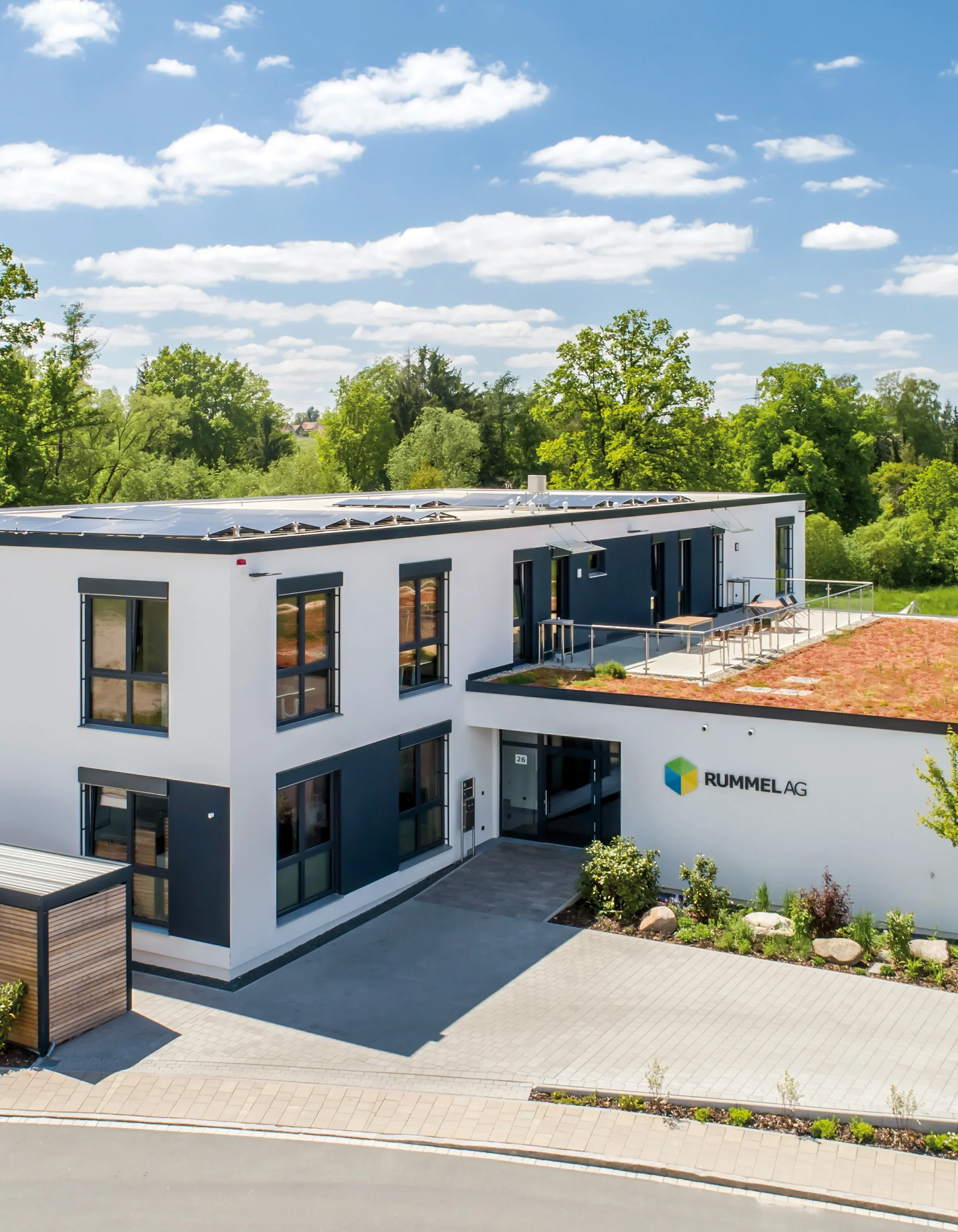 Modernes Bürogebäude mit begrüntem Dach, Solarmodulen und dem Schriftzug RUMMEL.AG.