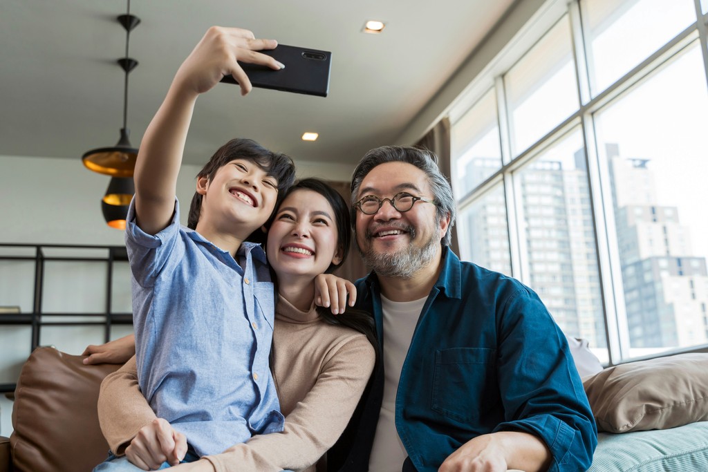 A cheerful family takes a selfie together in their modern, high-rise apartment with large windows, capturing a moment of happiness and connection in their urban home.