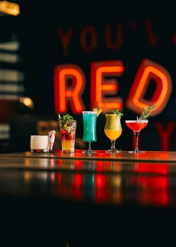 Colorful craft cocktails displayed on a bar counter with Red Rhino neon signage in the background