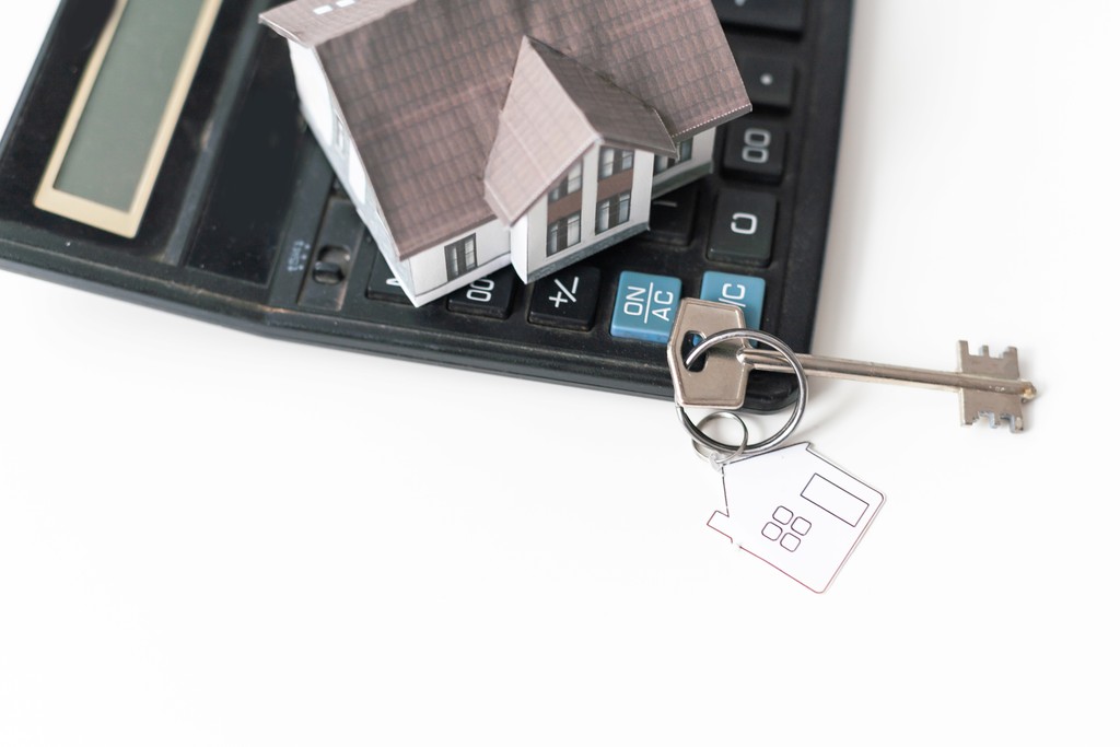 Huissleutel en hypotheekpapieren op rekenmachine – hypotheek oversluiten voor lagere maandlasten