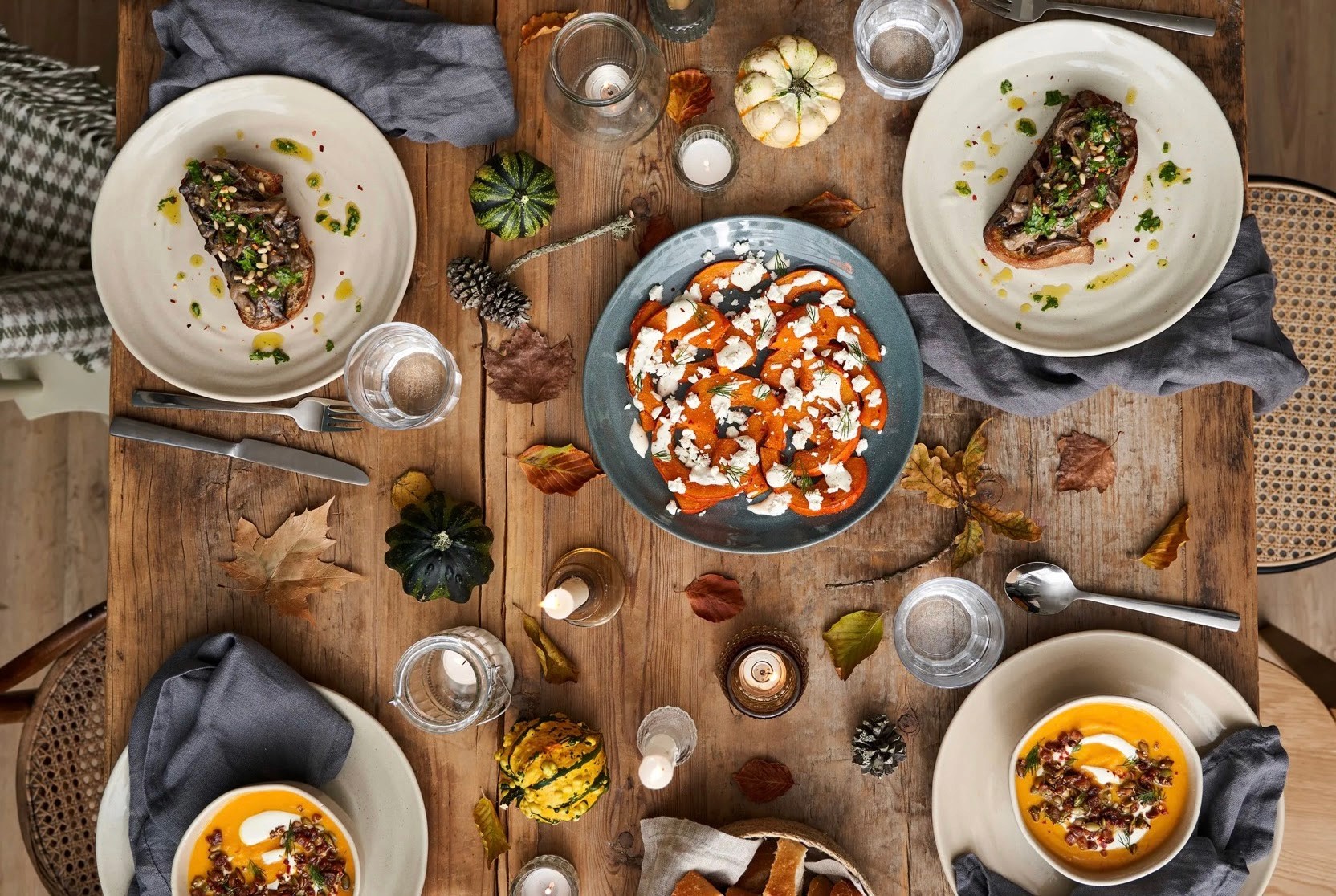 Vue aérienne d'une table en bois rustique dressée avec assiettes et bols en grès beige et bleu, velouté de potiron et salade de courge rôtie, décor automnal