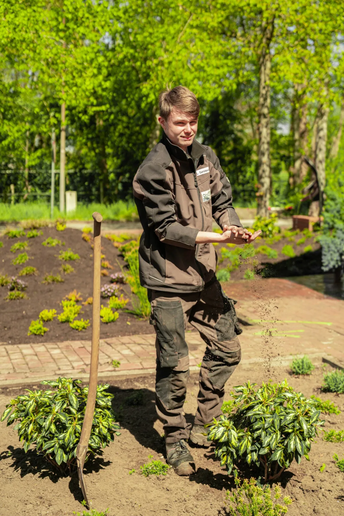Junger Gärtner lässt lächelnd Erde durch die Hände rieseln in einem angelegten Beet