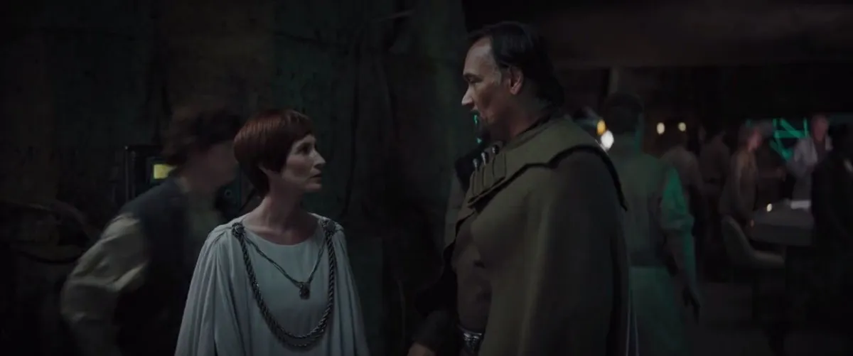 Mon Mothma and Bail Organa converse in a dimly lit Rebel base in Rogue One, surrounded by operatives preparing for action