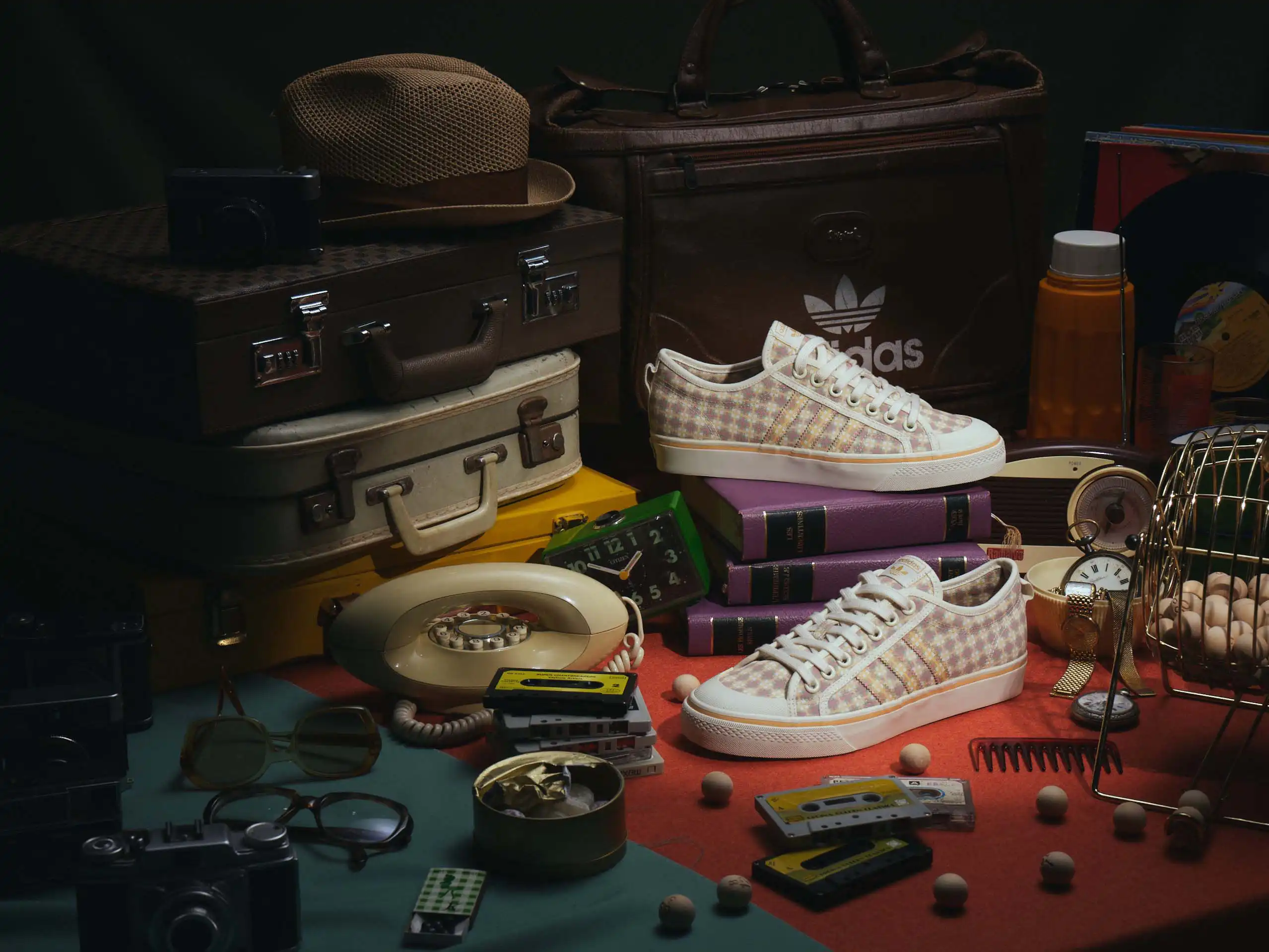 Michiel Spijkers still life photography for Adidas Vintage Club, featuring vintage sneakers spotlighted among suitcases, a rotary telephone and leather travel bags in a thrift-shop-style scene.
