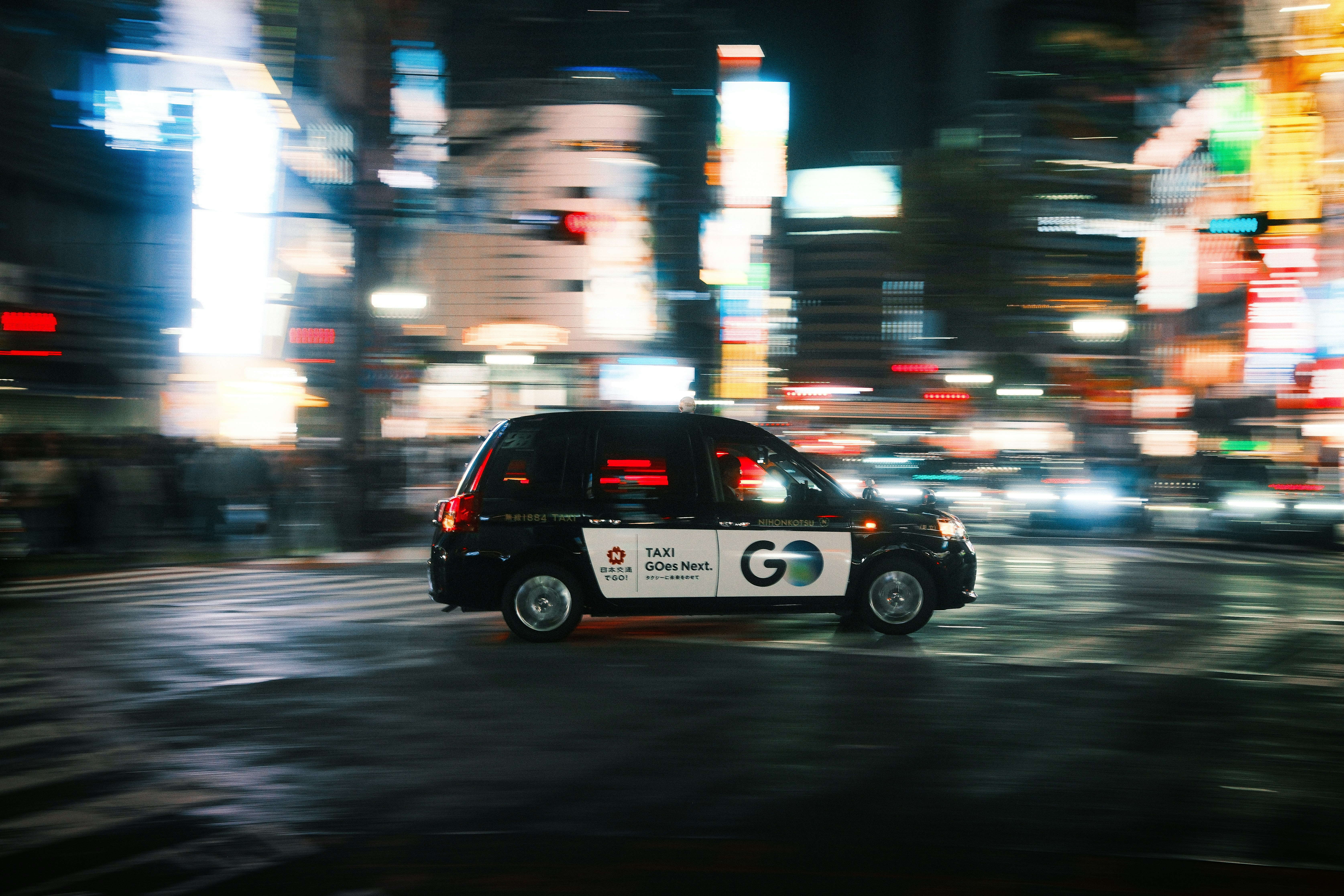 A taxi speeds through a blurry city street at night.