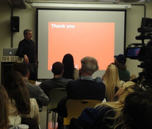 A photo of a group of people listening to a lecture and watching a screen that has an orange projection on it with the white text that says: Thank You.
