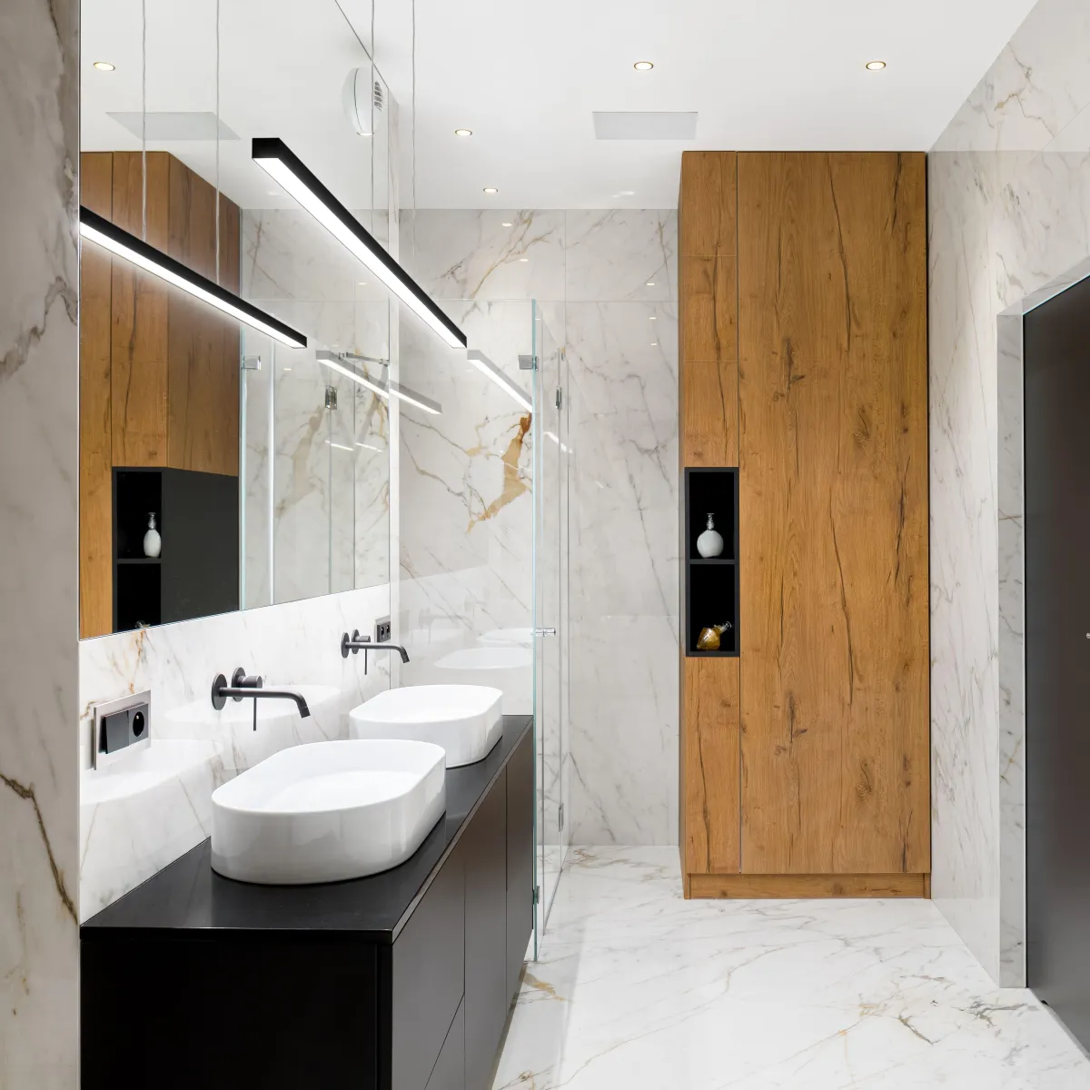 Elegant bathroom remodel by B&Y Reno Corp showcasing dual vessel sinks, marble walls, sleek wood cabinetry, and matte black fixtures.