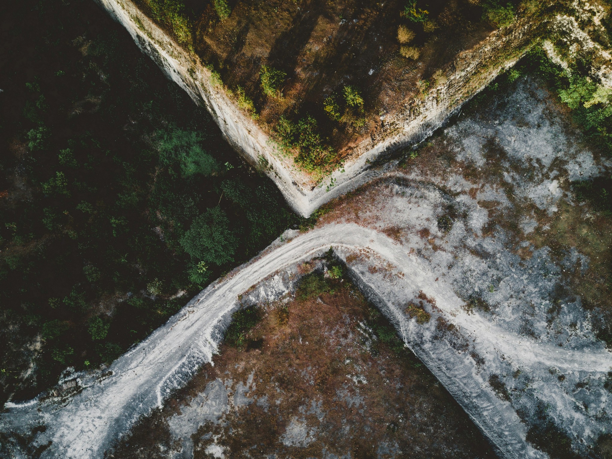 Aerial view of an intersecting dirt pathway forming an X-shape surrounded by lush greenery and arid, rocky terrain, illustrating a contrasting landscape.