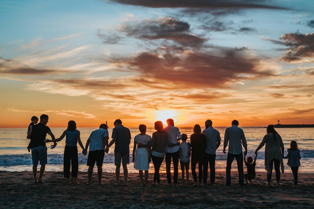 A large family gathered on the beach, holding hands and watching a stunning sunset over the ocean. The scene captures a sense of togetherness, love, and the beauty of nature, perfect for moments of family bonding and cherished memories.