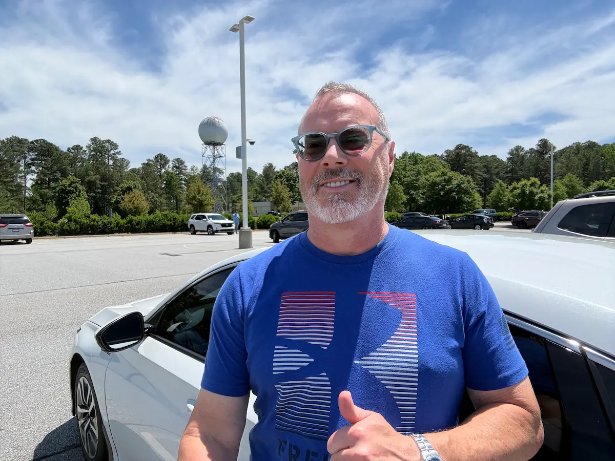 Stu standing beside his white Honda Accord in a sunny parking lot during the day, smiling while wearing sunglasses and a blue shirt.