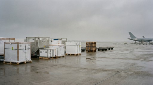 Insulated shipping containers sit unattended on an airport tarmac under overcast skies, exposed between transport stages.