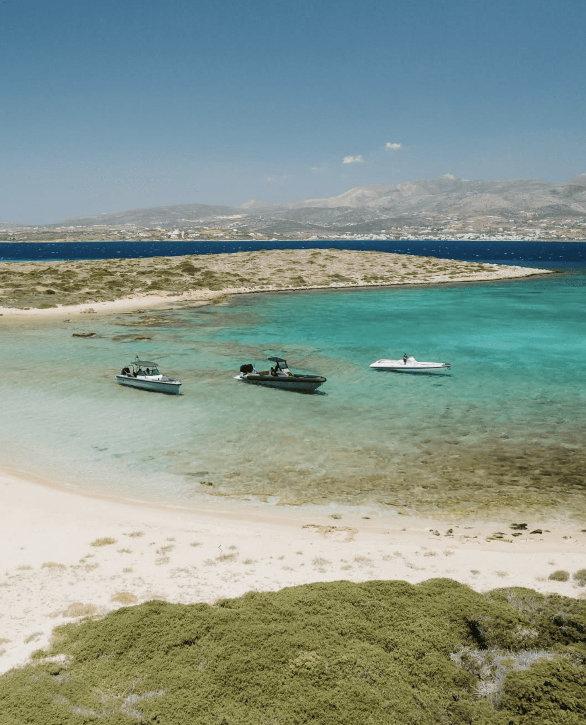 Aerial view of three motor yachts anchored in crystal-clear turquoise waters of the Aegean Sea.