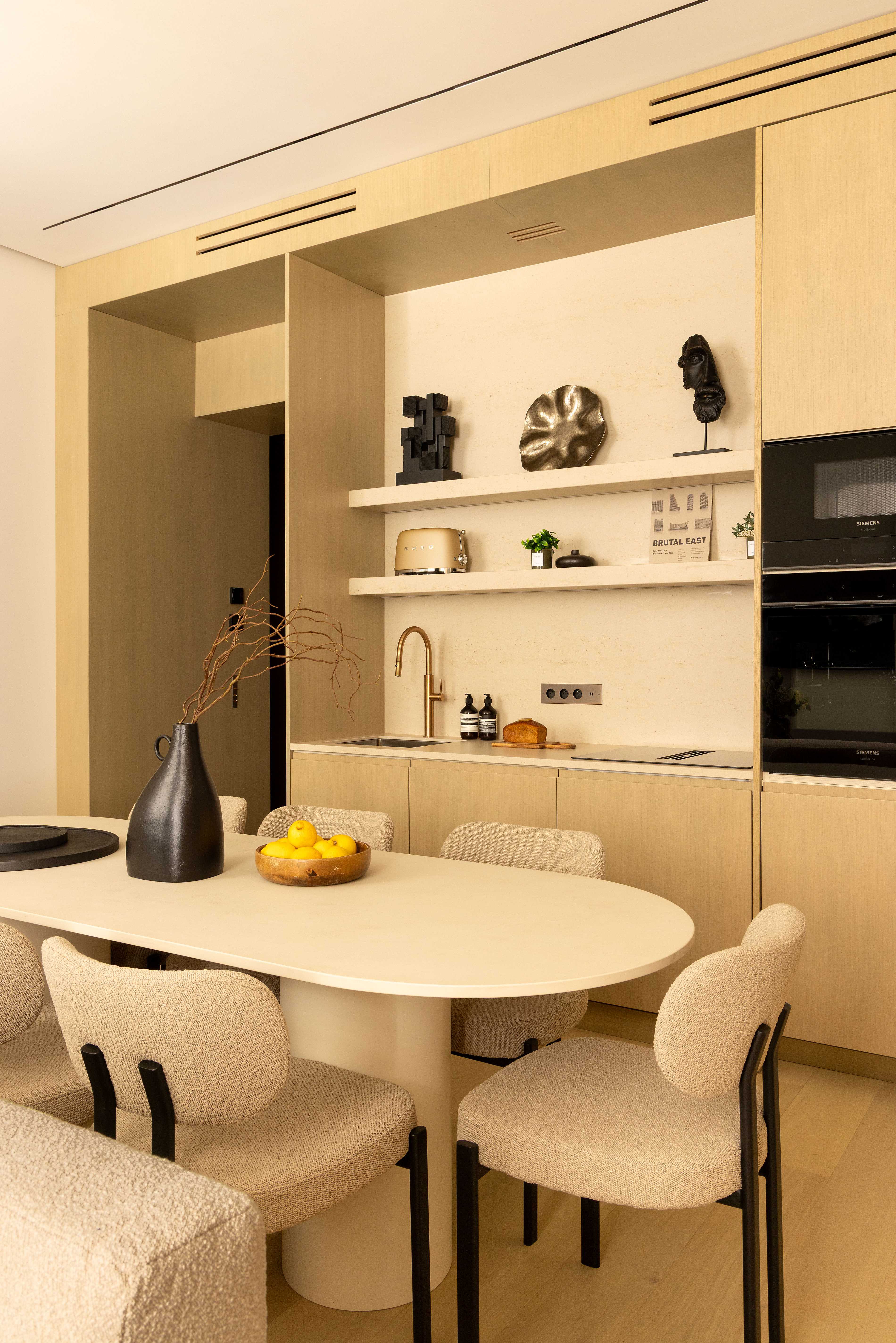 Vue rapprochée de la cuisine avec table ovale, chaises bouclette et étagères avec objets d'art