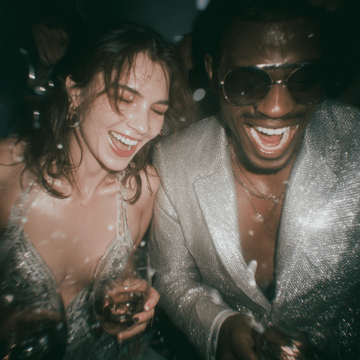 Close-up of a man in a sequined jacket and a woman laughing together at an evening event.