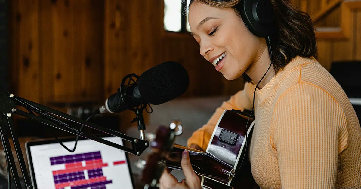 Singer-songwriter recording music at home, playing acoustic guitar and singing into a microphone.