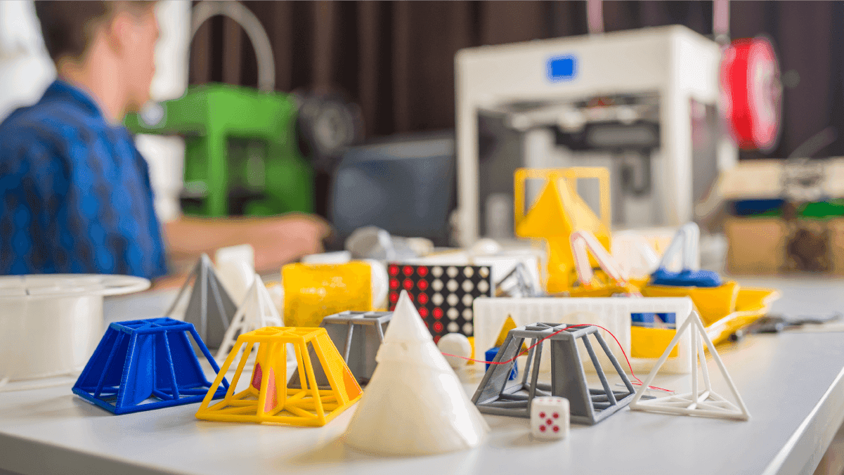 Colorful 3D-printed physical model prototypes in various geometric shapes displayed on a workshop table
