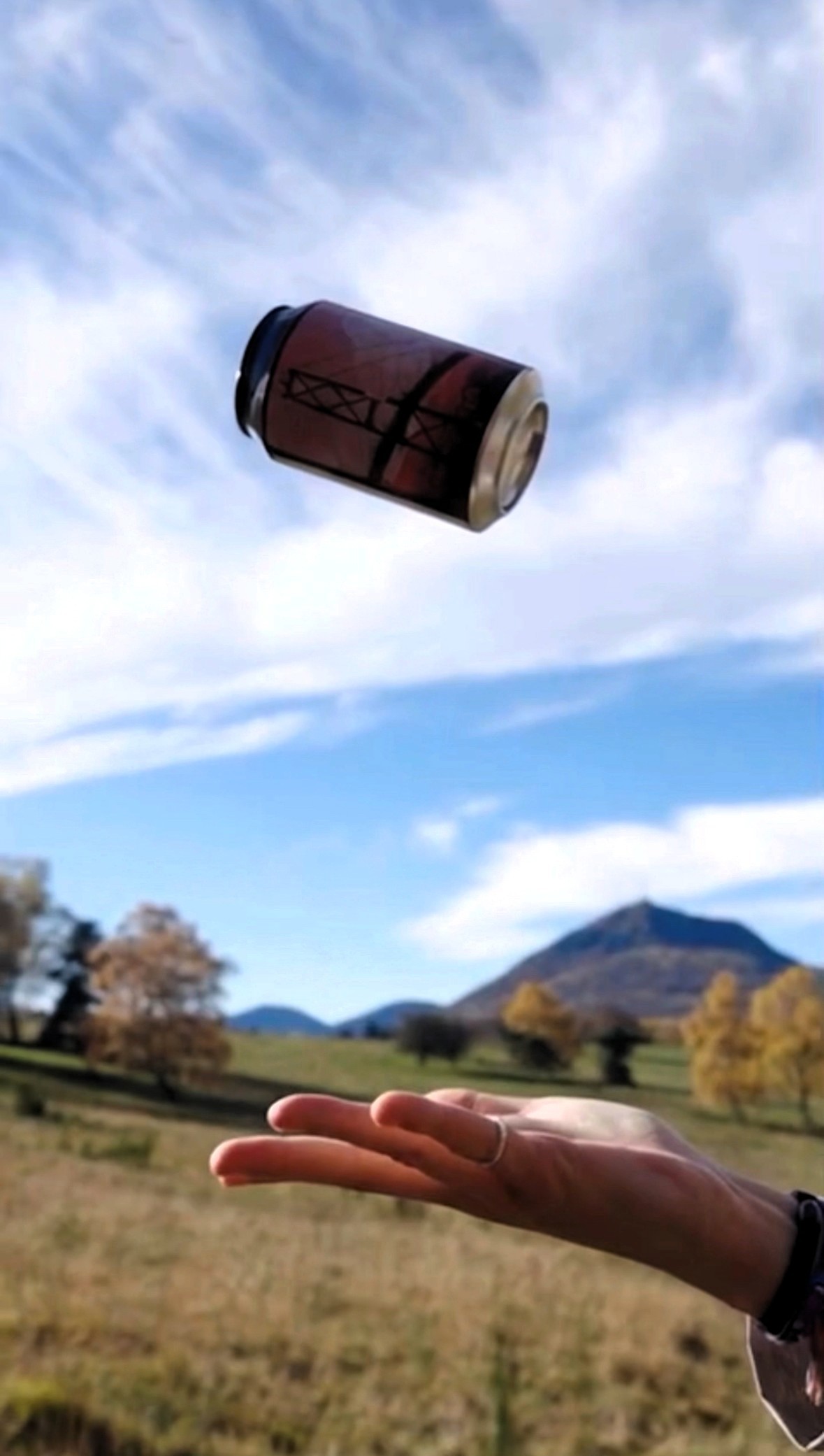 Main qui jette une canette dark lab en l'air avec Puy de Dôme en arrière-plan